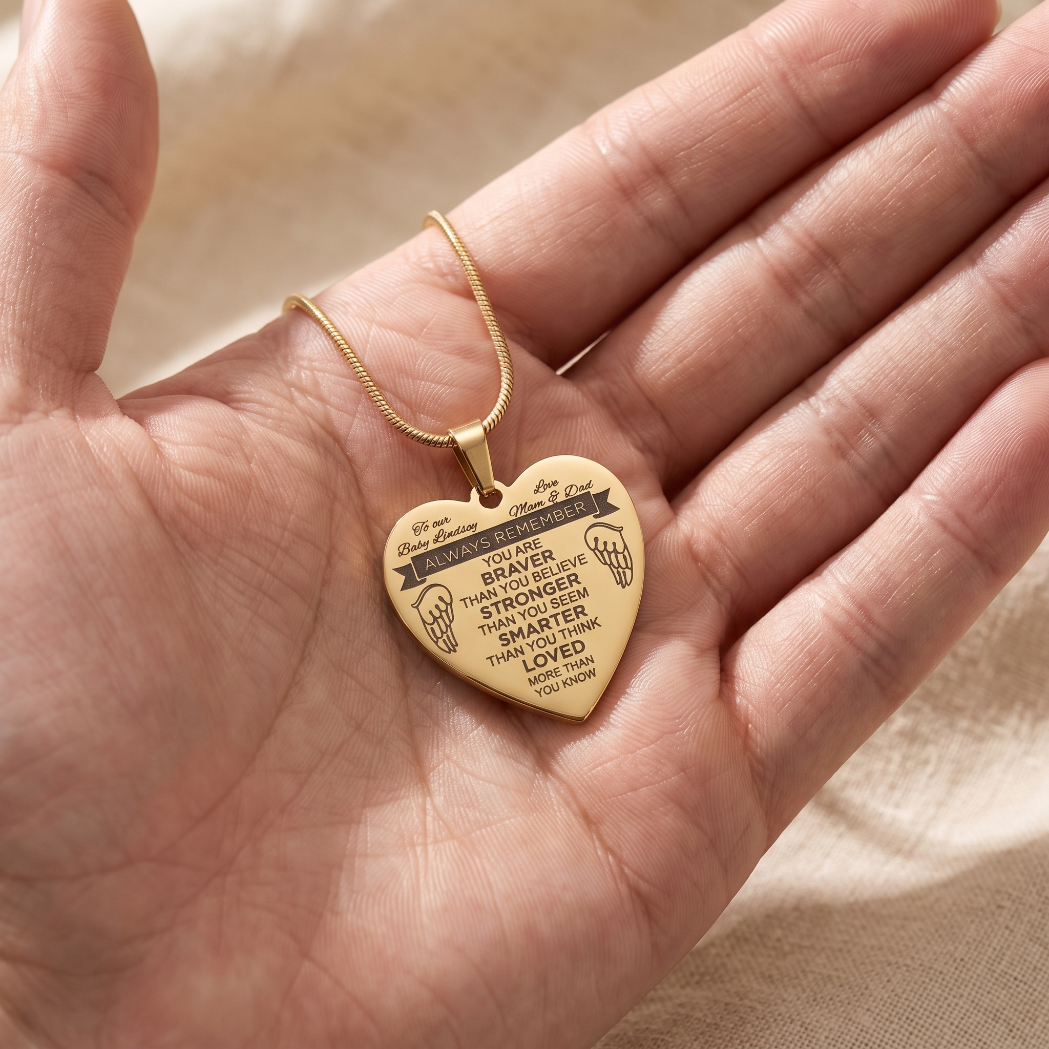 A woman's hand resting on an engraved name pendant at her collarbone in soft morning light