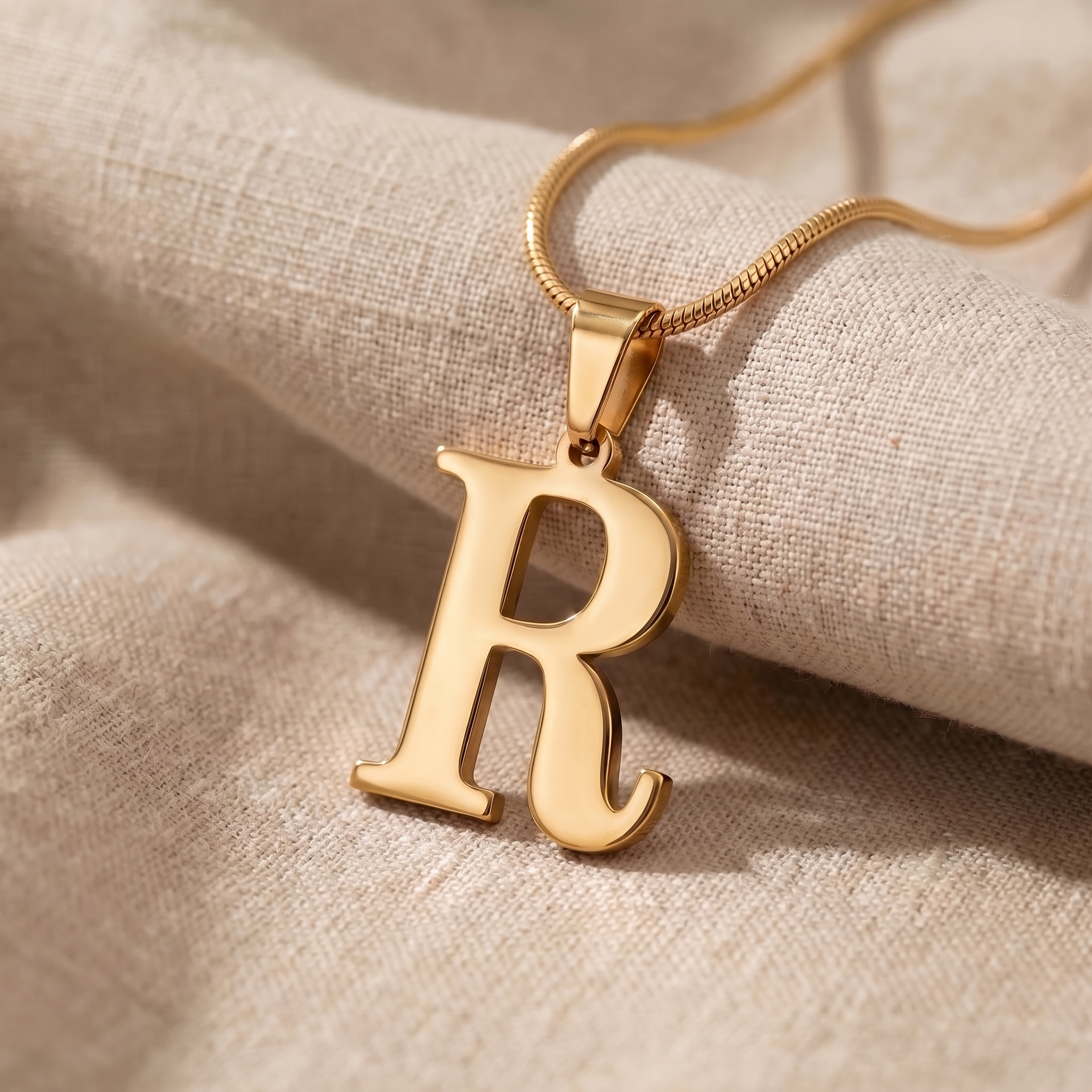 A letter pendant and a longer name pendant laid side by side on linen