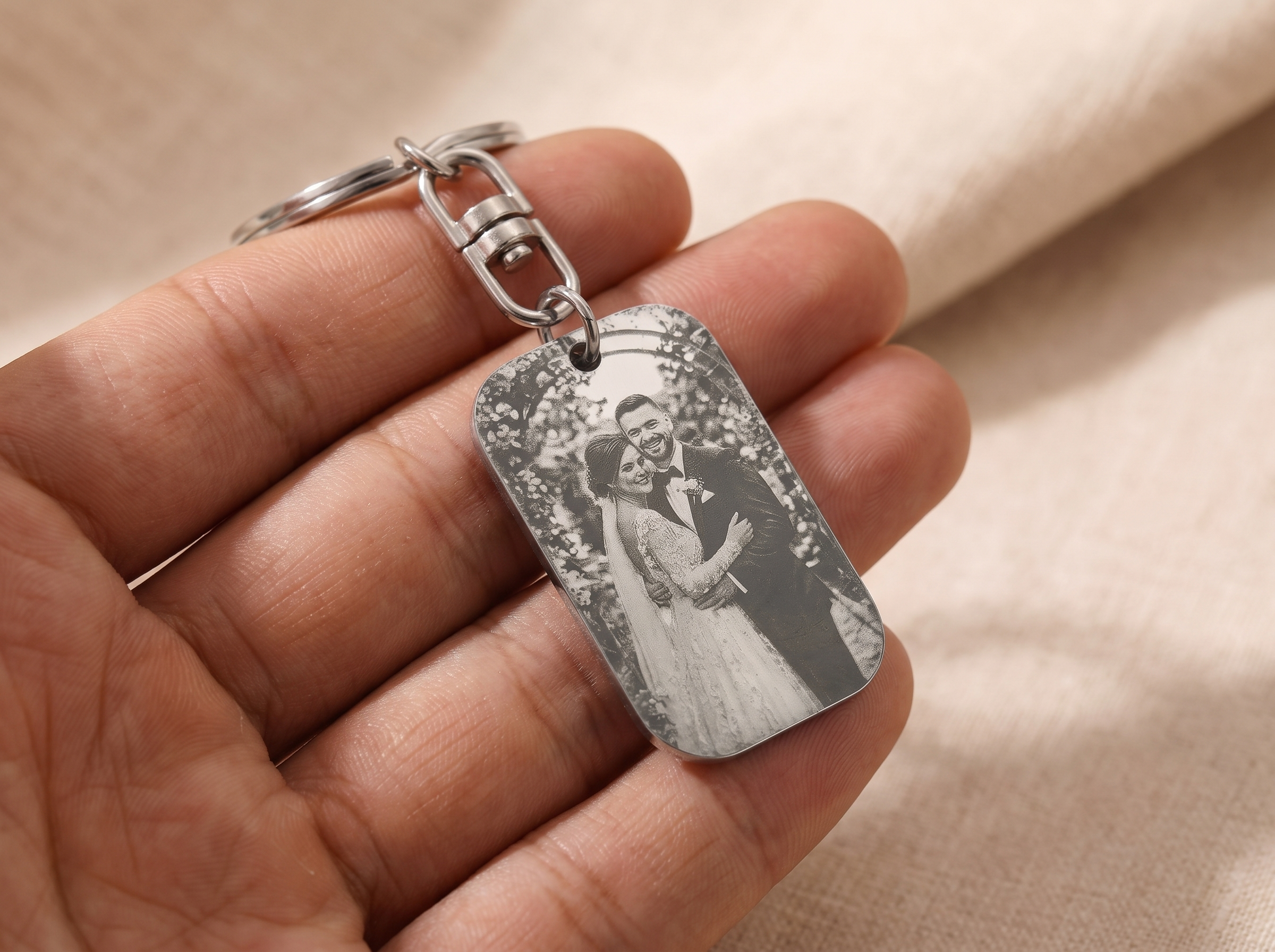 Close-up of a name and date engraved into a silver tone keyring tag held between two fingers