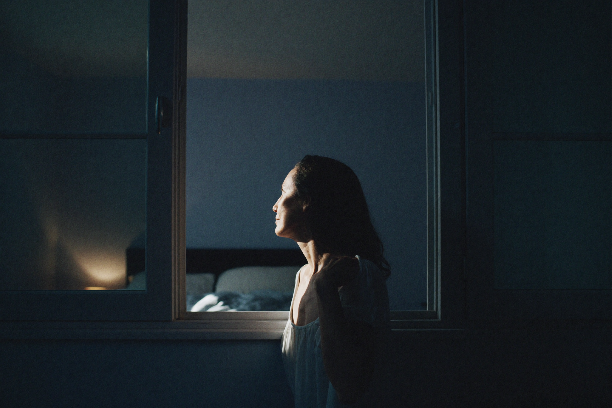 A woman at a bedroom window at night