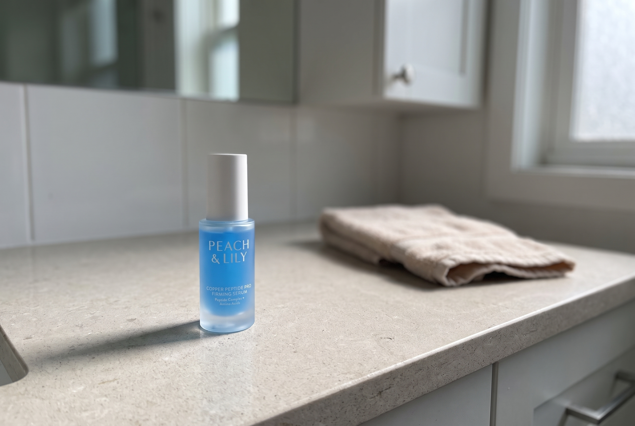 Peach and Lily Copper Peptide Pro Firming Serum bottle on a light stone counter