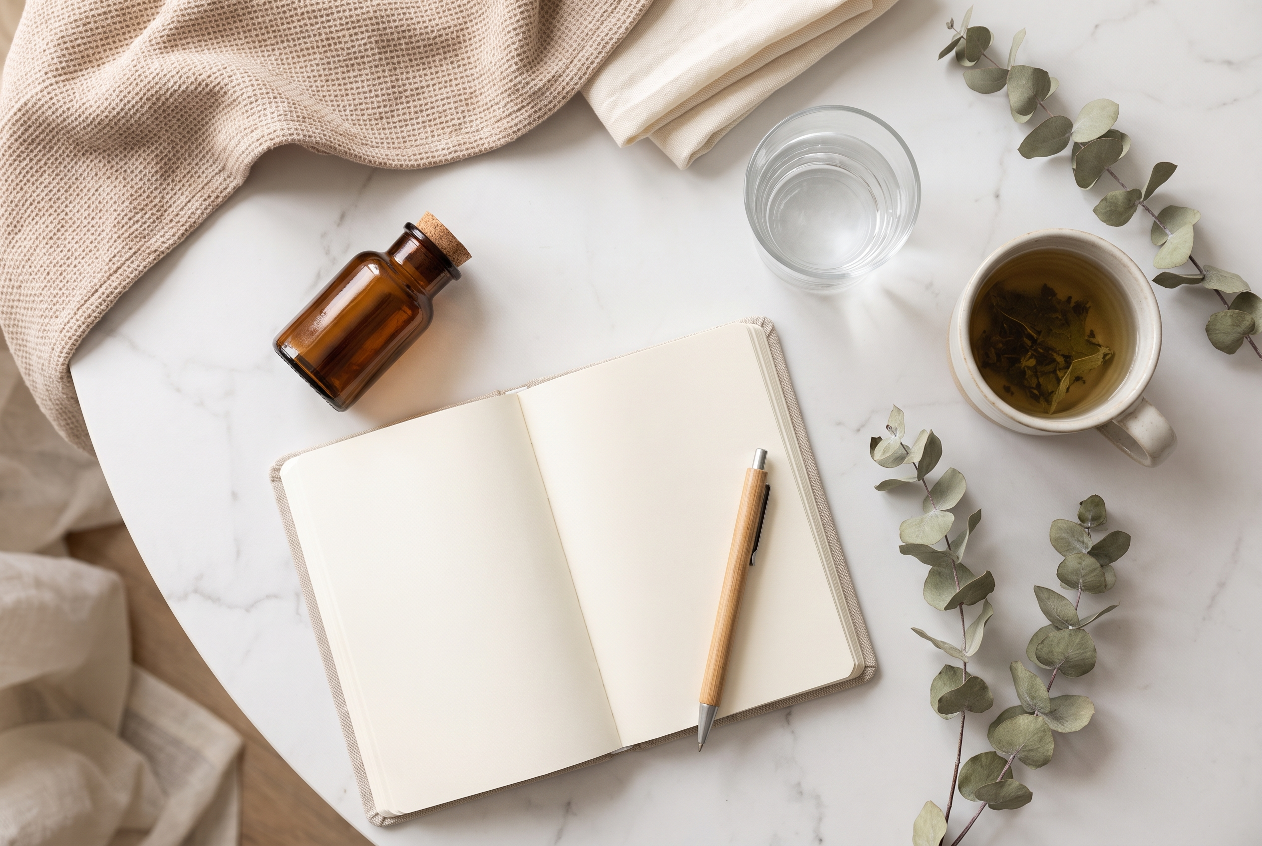 A calm wellness flat lay with a small amber vial, a notebook, and a glass of water