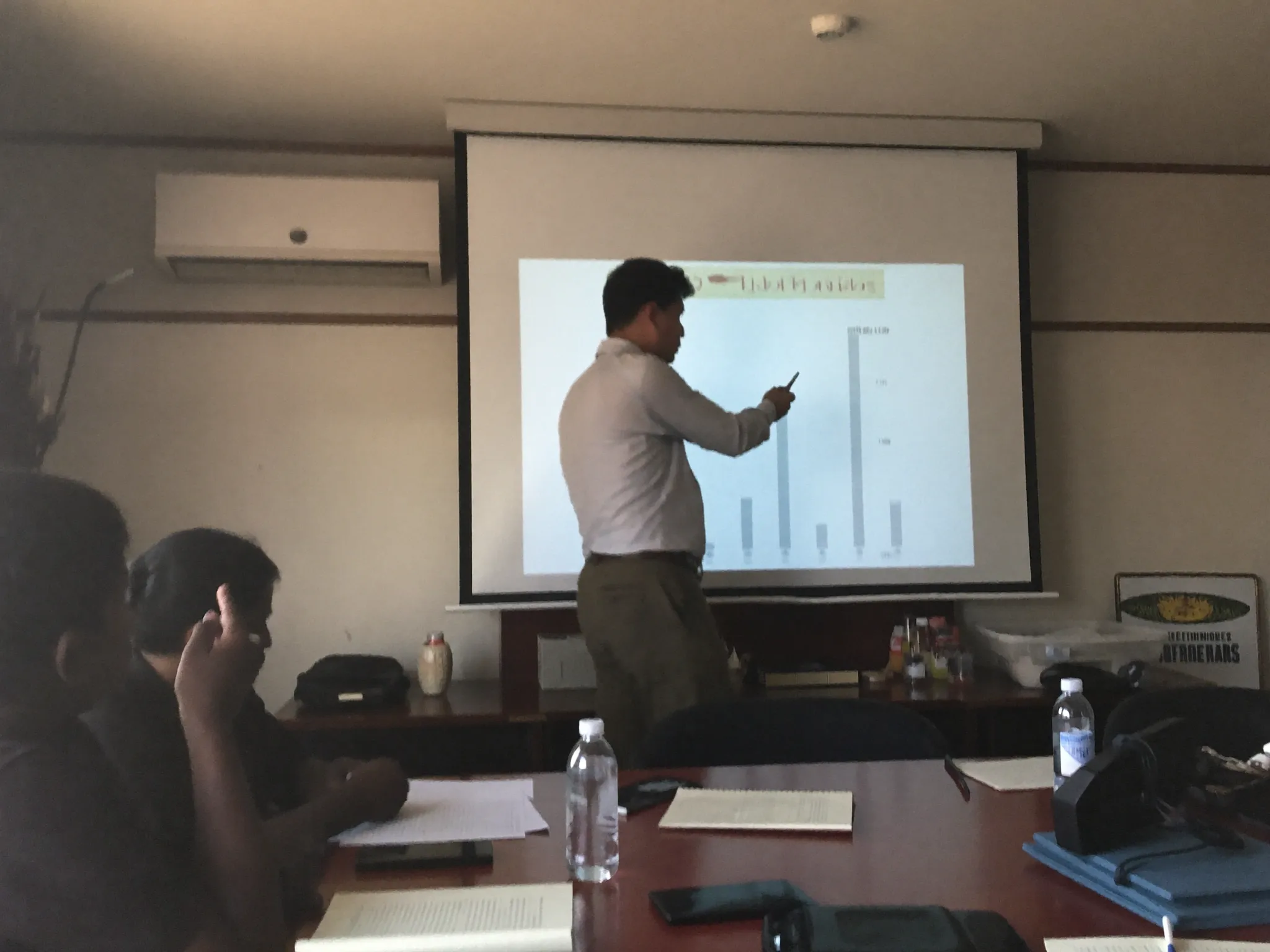 Officials reviewing charts on a screen in a meeting room