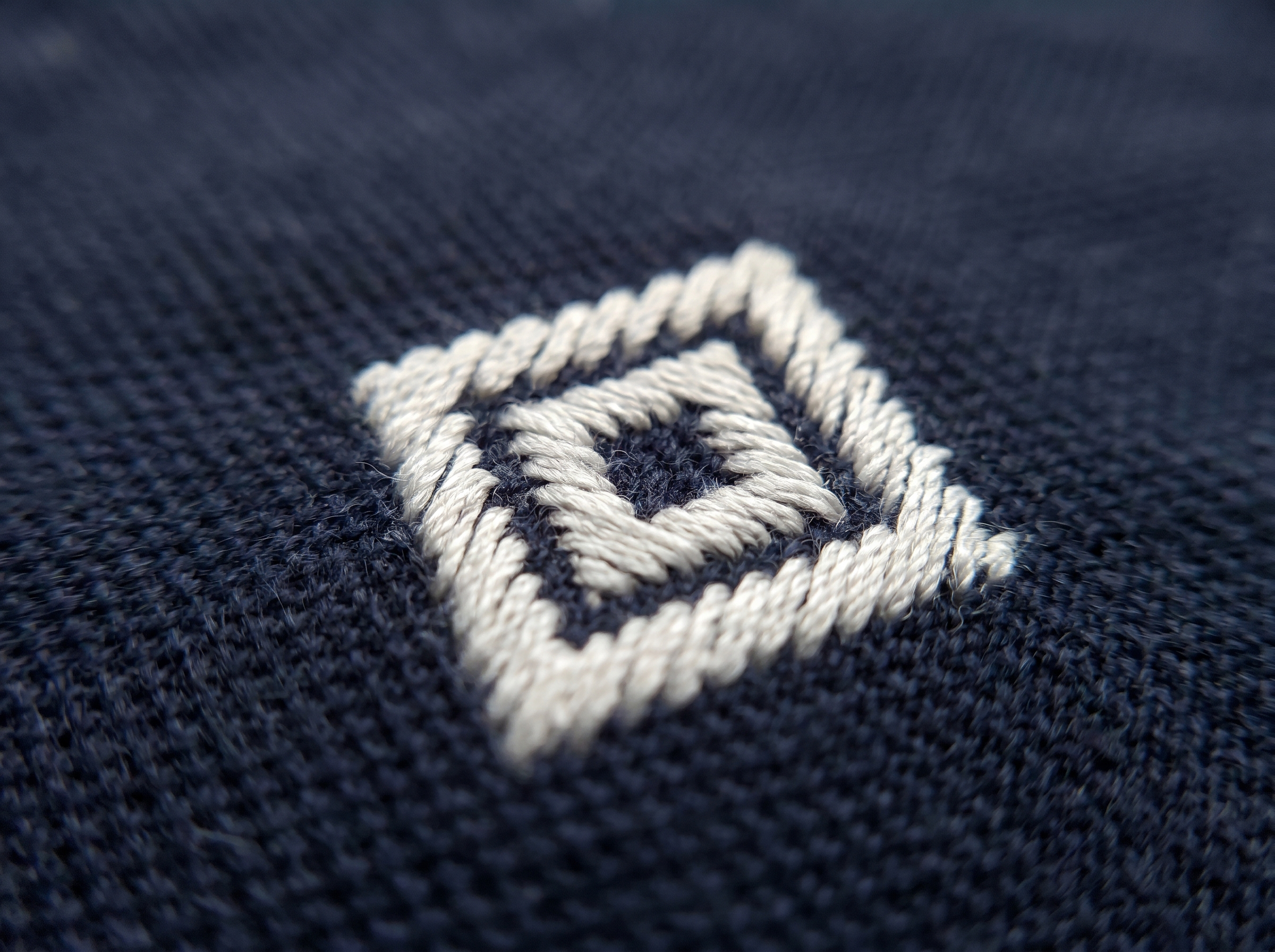 Custom embroidered logo close-up on left chest of navy polo shirt - thread detail and stitch quality visible