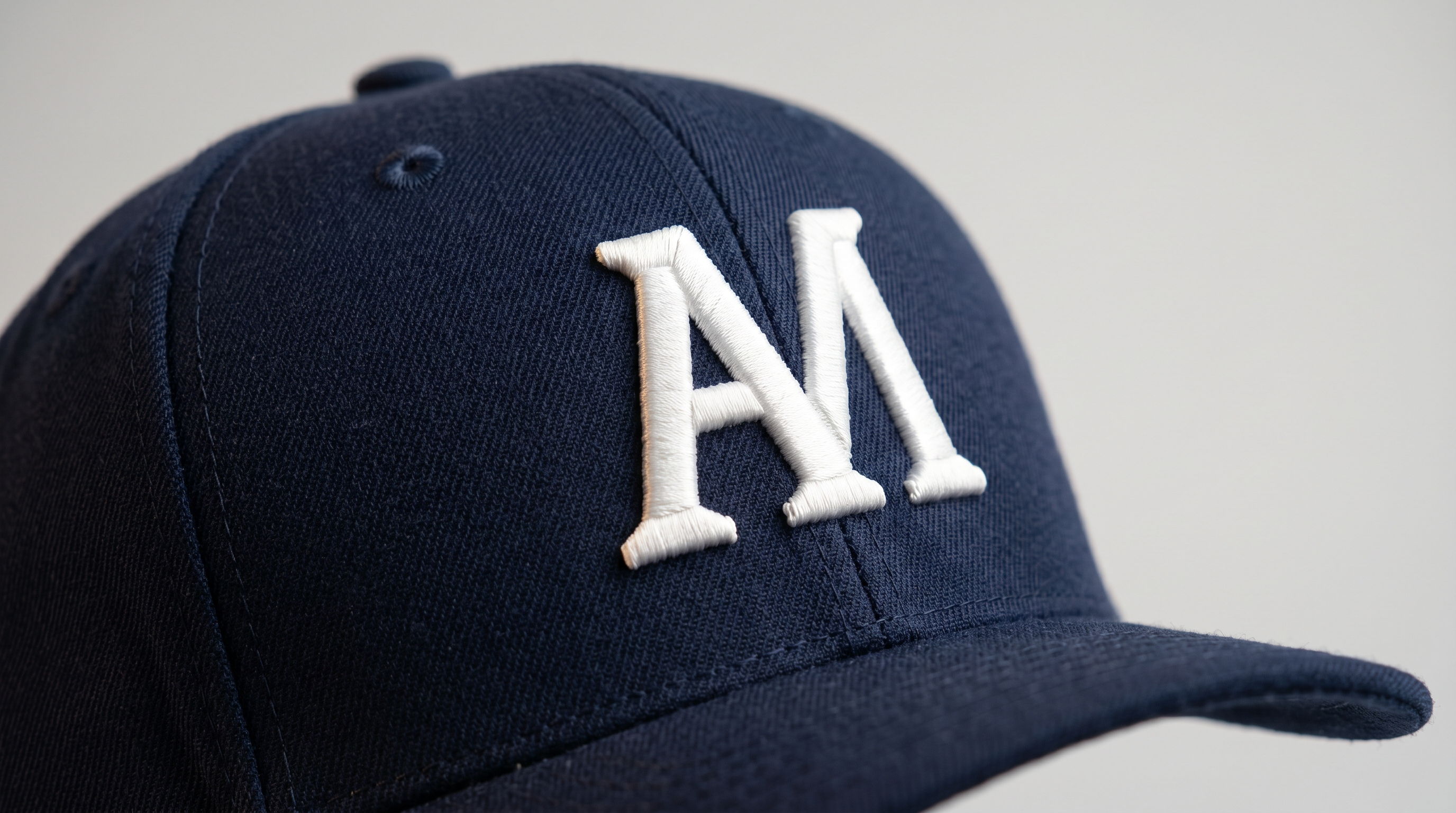 Macro close up of 3D puff embroidery on a navy structured snapback, showing the raised satin stitches over foam underlay catching directional light