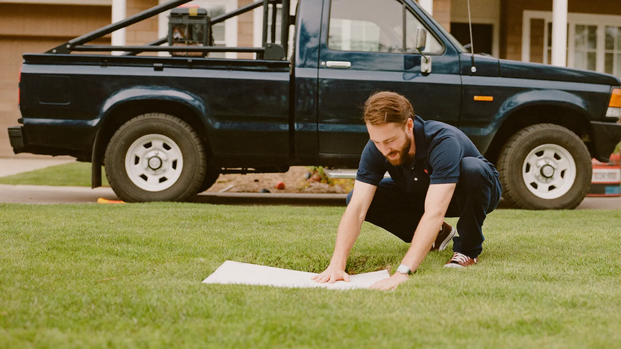 A contractor placing a clean yard sign in a freshly finished lawn with his work truck behind him