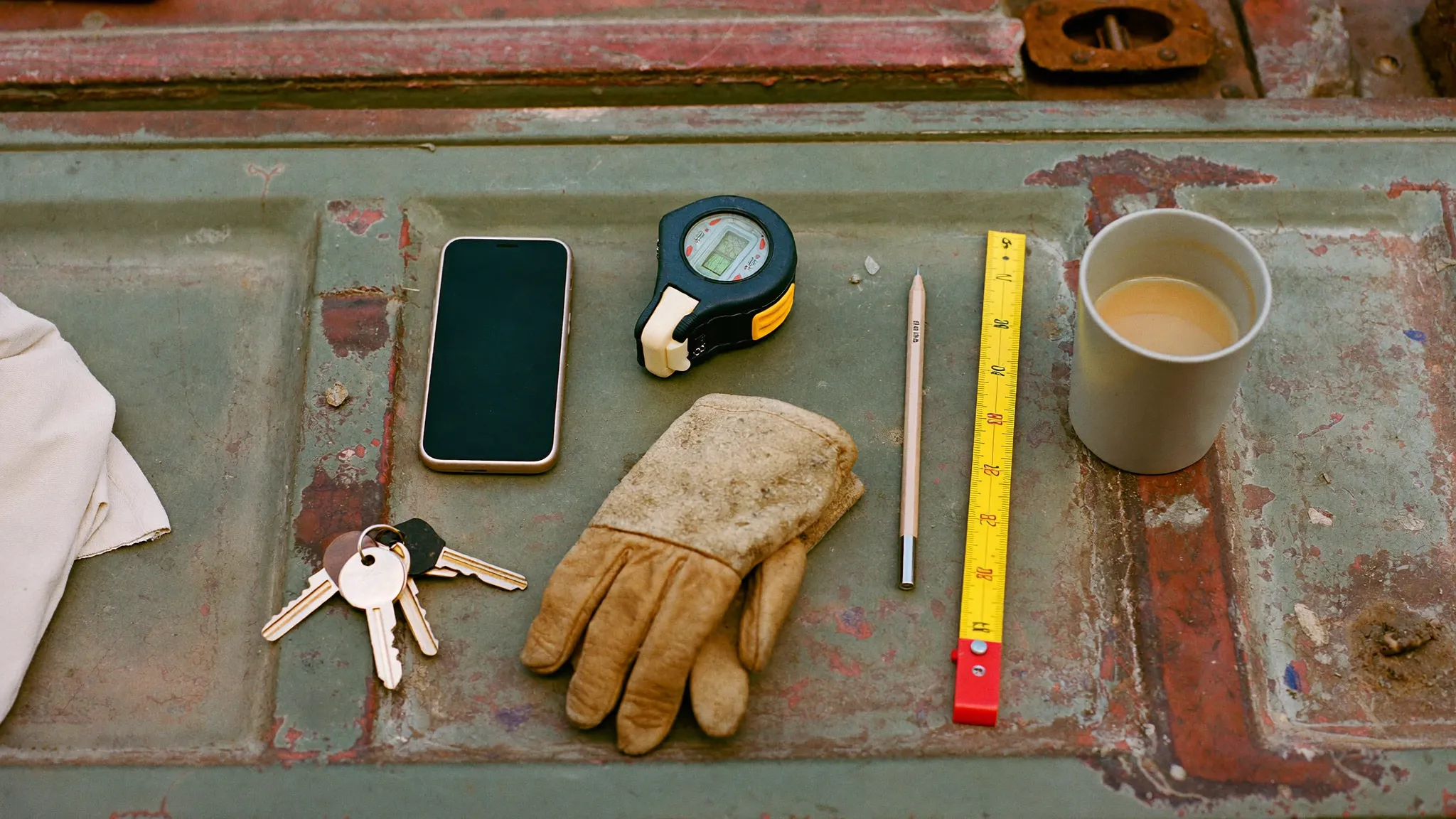 A contractor's phone, tape measure, work gloves, keys and coffee laid out on a truck tailgate