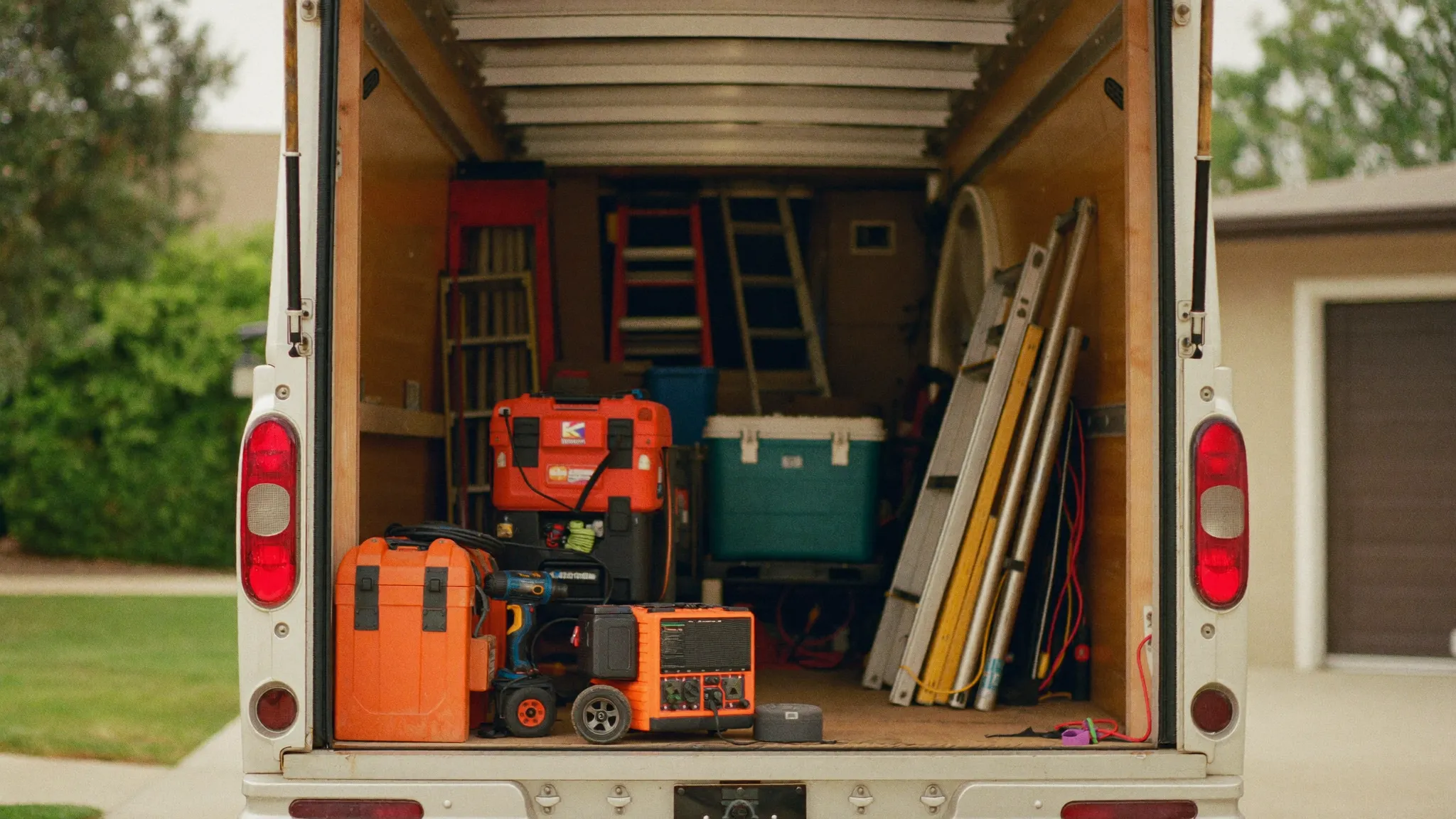 The open back of a contractor's work trailer packed with tools and equipment