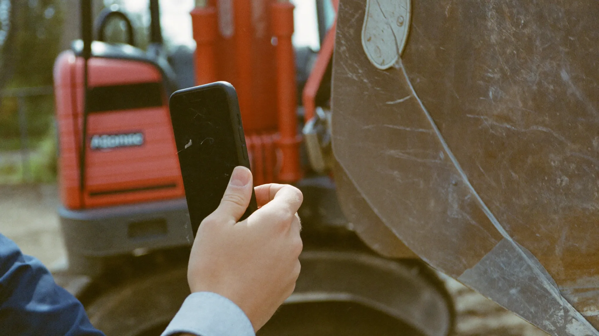 A contractor photographing a scratch on a rented excavator bucket during a delivery inspection