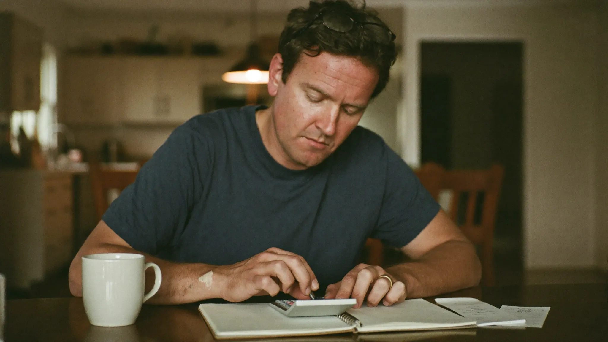 A painting contractor at his kitchen table in the evening working out his marketing budget with a calculator and notebook