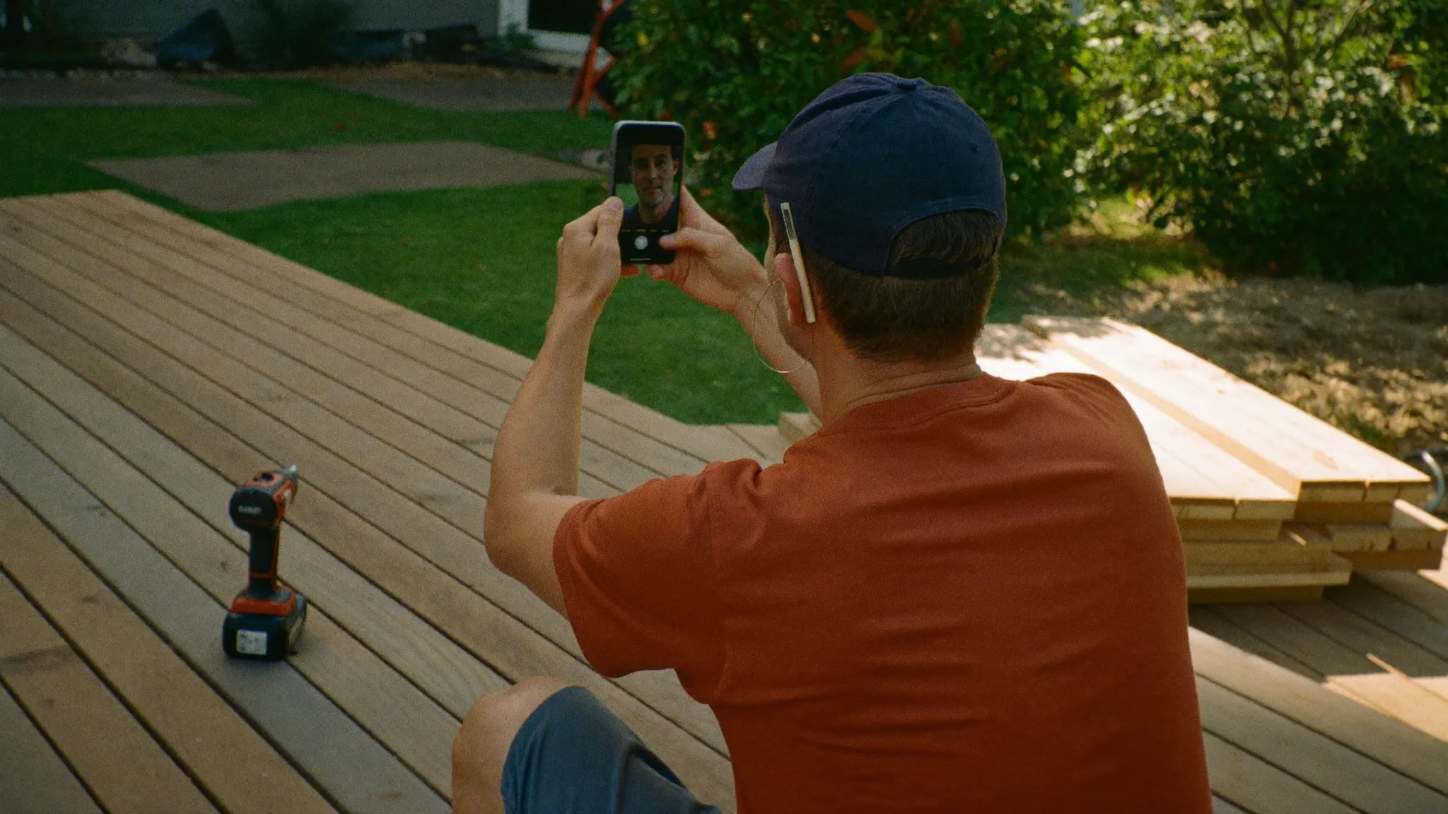 A deck builder photographing a freshly finished deck with his phone in the late afternoon sun