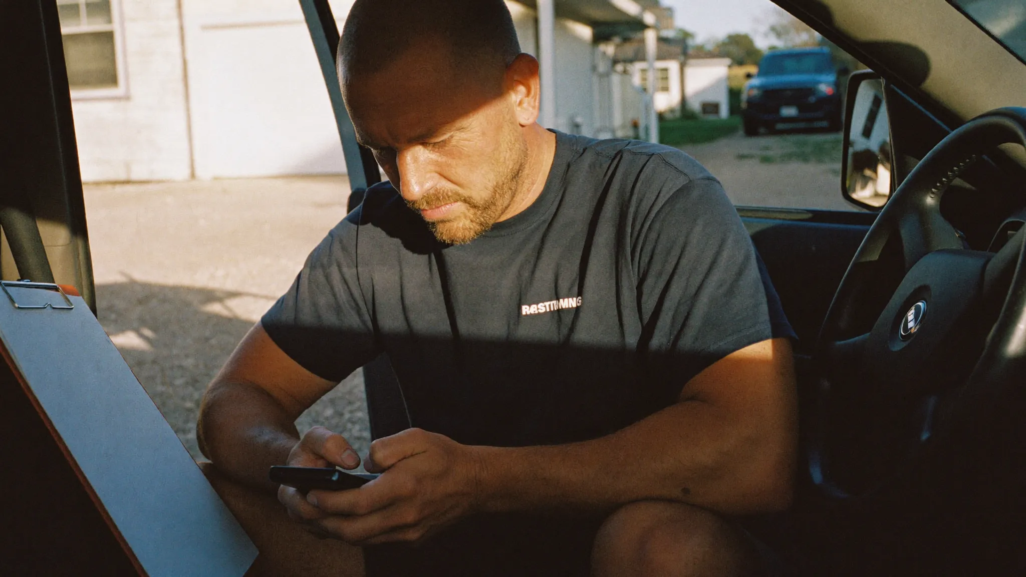 A remodeling contractor sitting in his open truck door reviewing his phone in late afternoon light