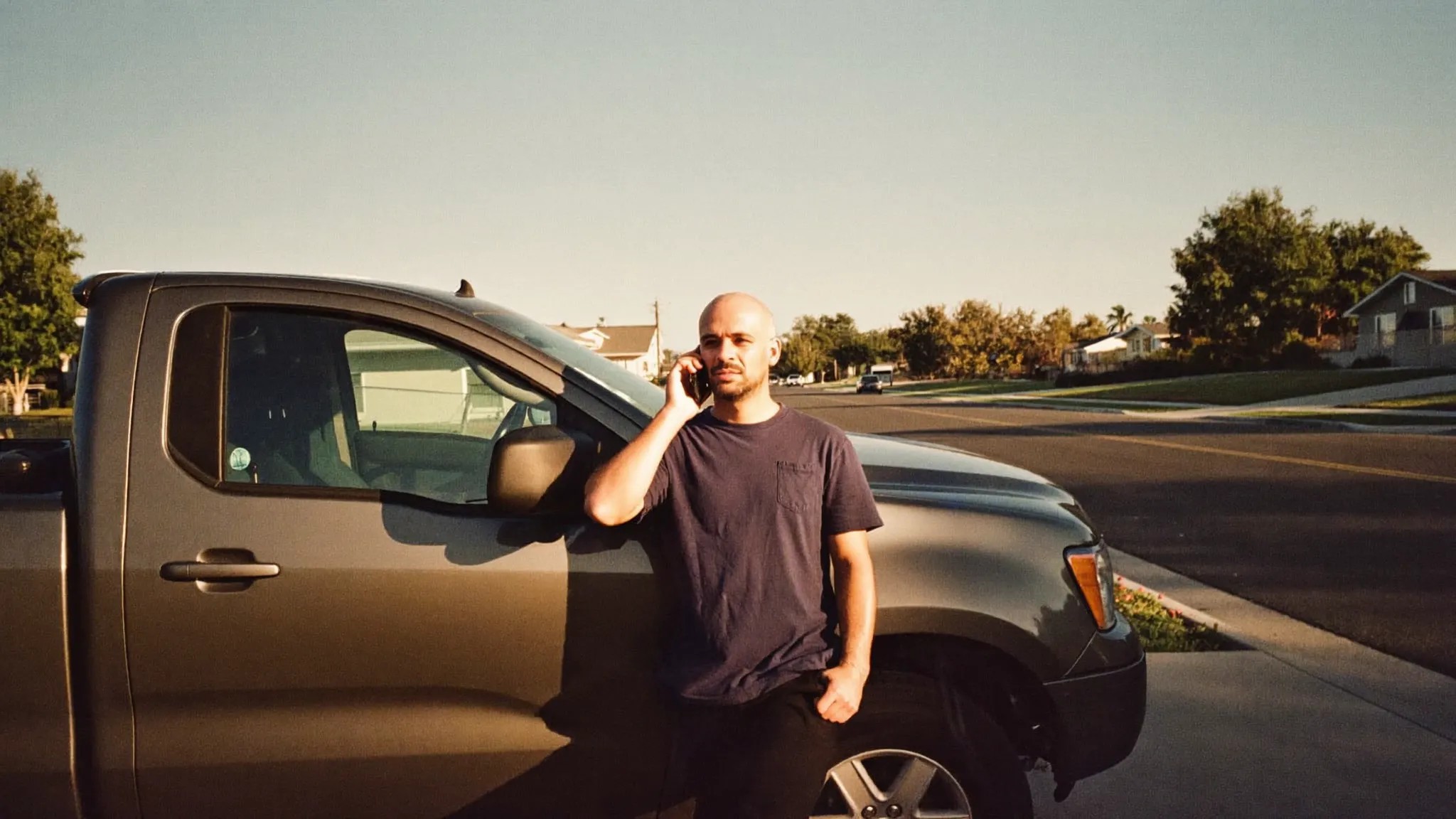 A residential contractor leaning against his pickup truck taking a phone call from a new lead at golden hour