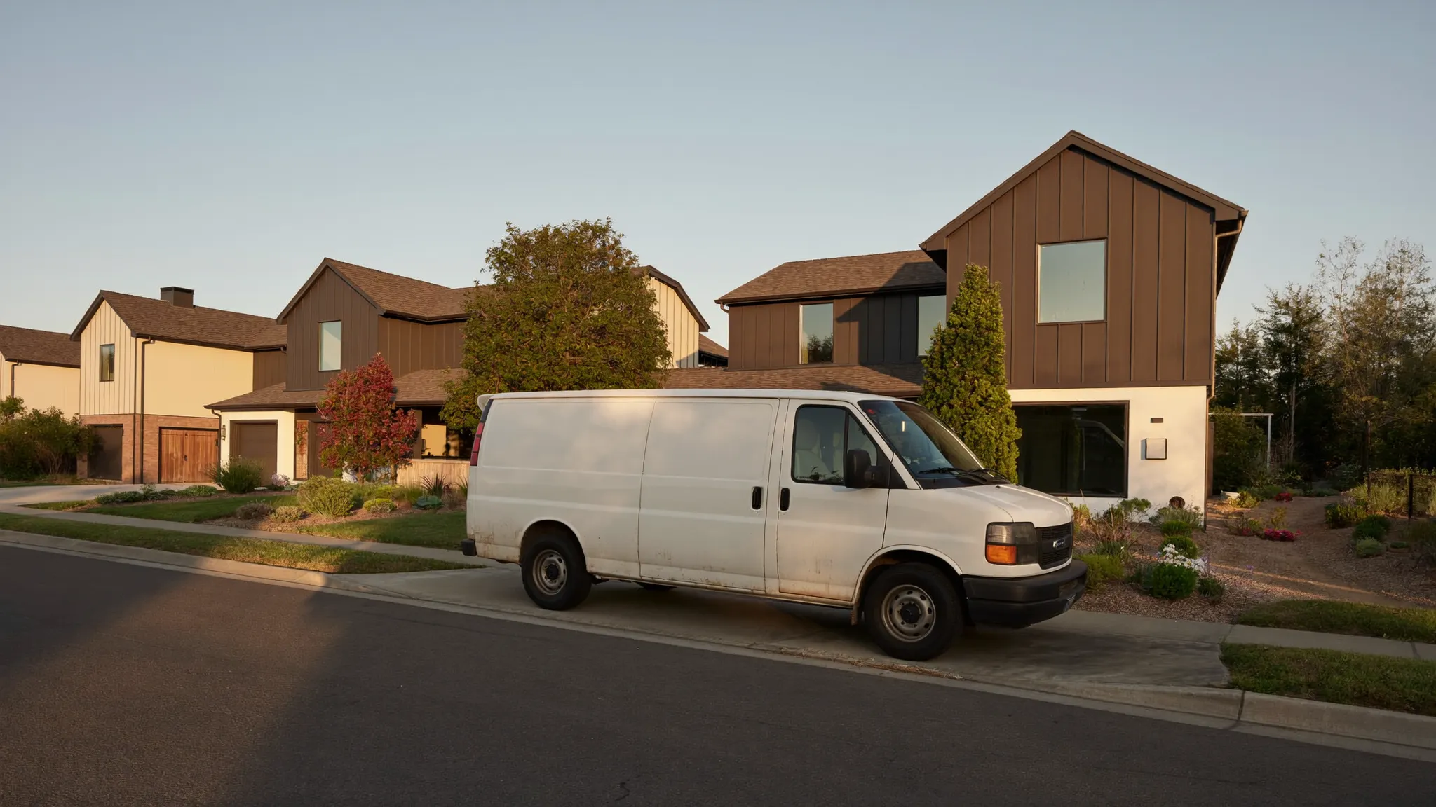A newly finished two story suburban home at golden hour with a plain work van parked at the curb