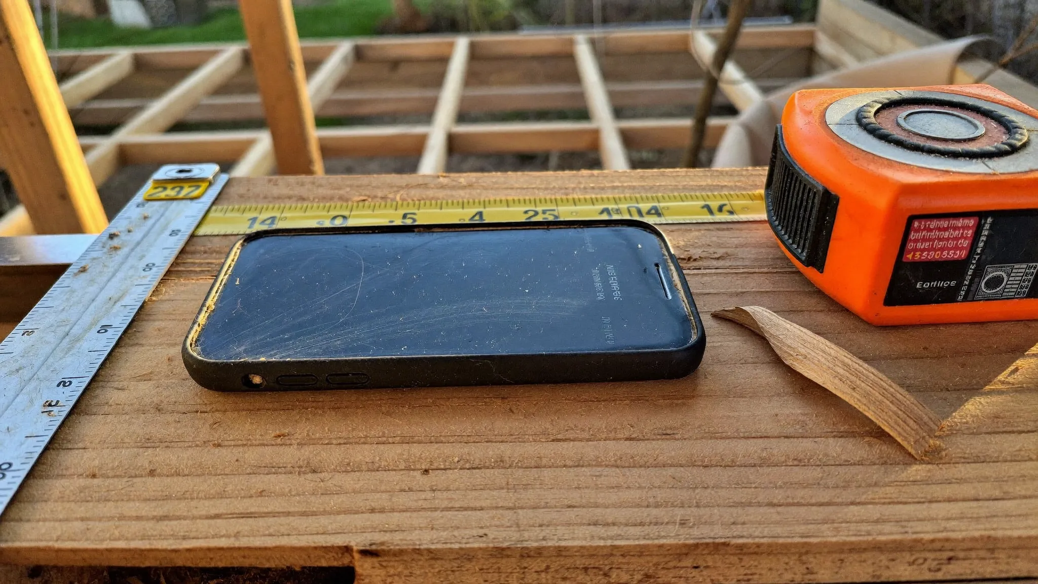 A smartphone resting on a stack of cedar deck boards beside a tape measure and chalk line at an unfinished deck build