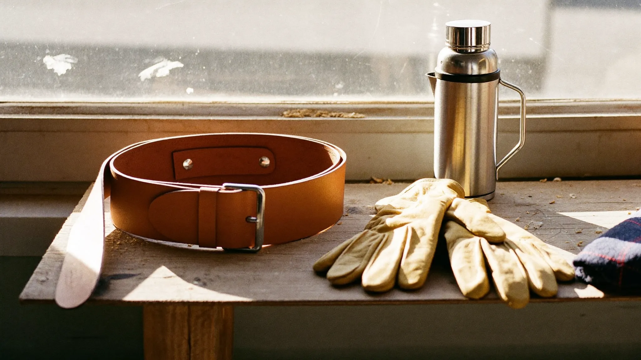 A brand-new leather tool belt and stiff work gloves laid out on a workbench in morning light