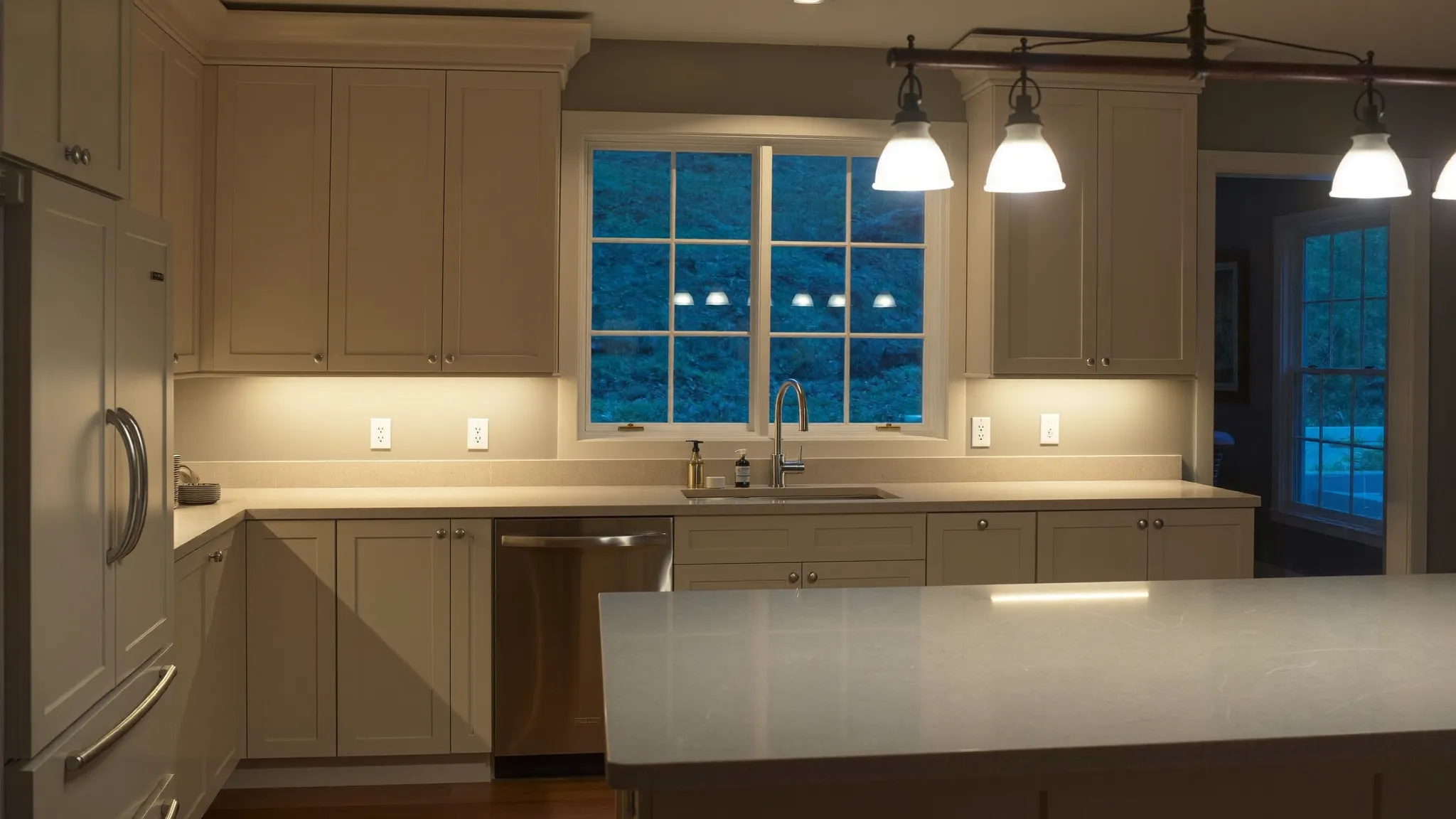 A newly remodelled kitchen at dusk with warm under cabinet lighting and pendant lights over the island