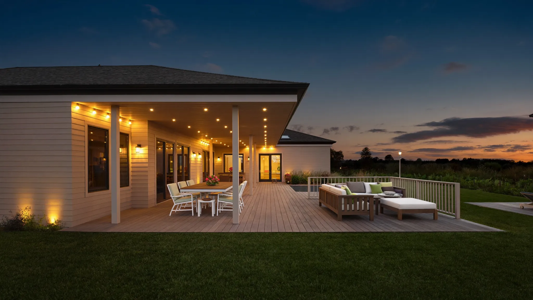 A newly finished covered deck and patio glowing with warm lights at dusk behind a suburban home