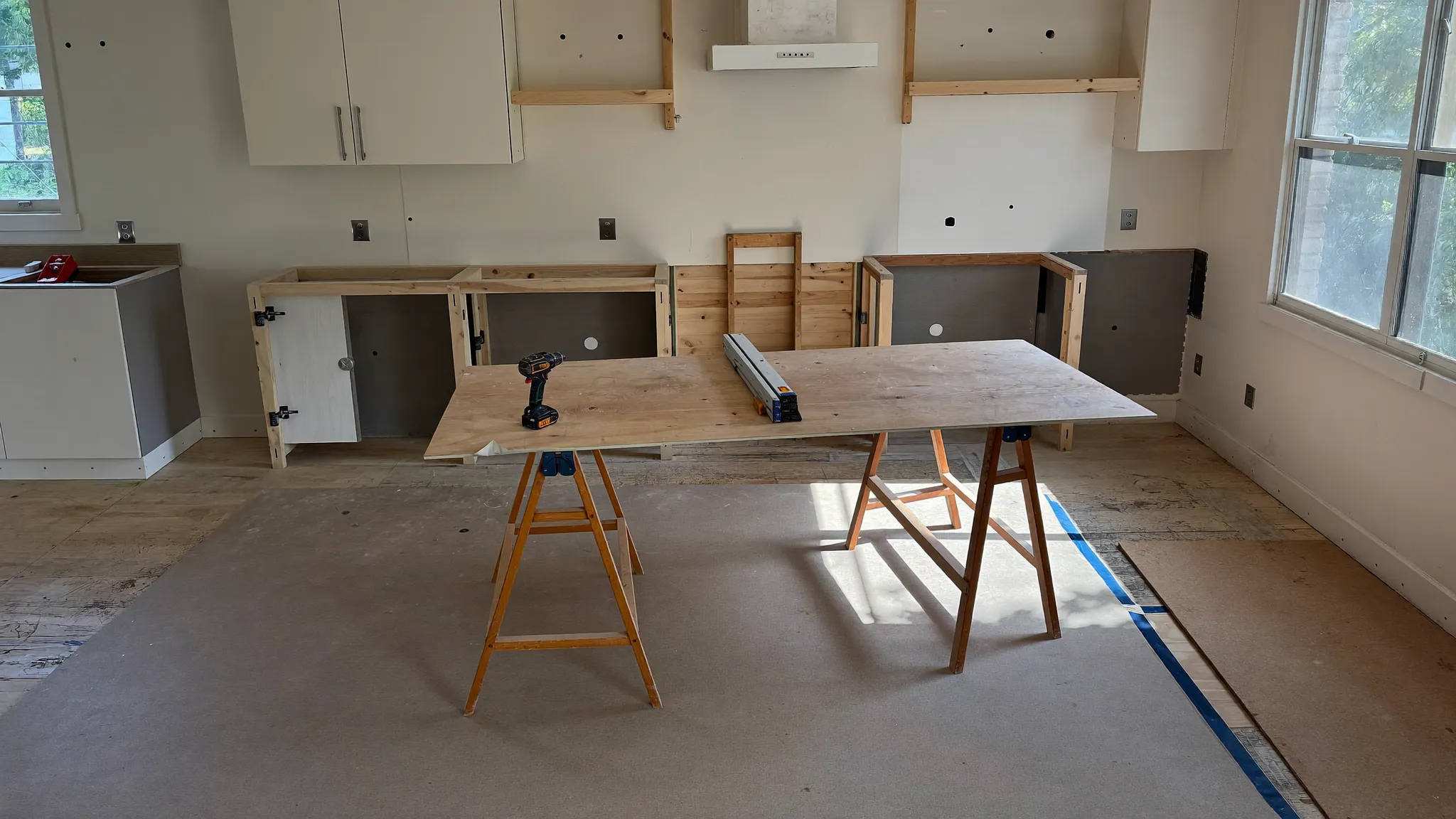 A kitchen mid remodel with new cabinets going in and a plywood sawhorse workbench in the foreground