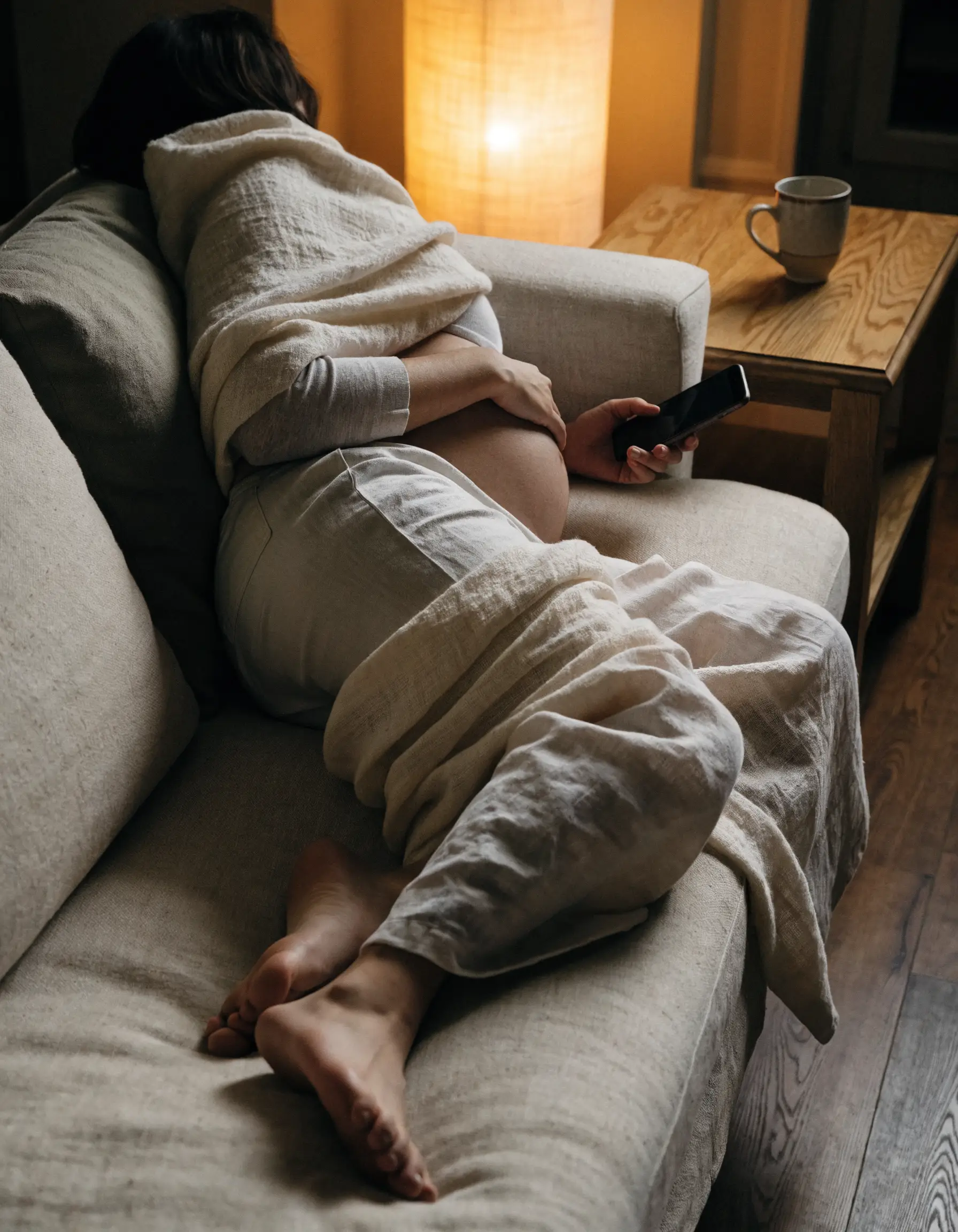 A woman resting on a linen sofa in soft evening lamplight