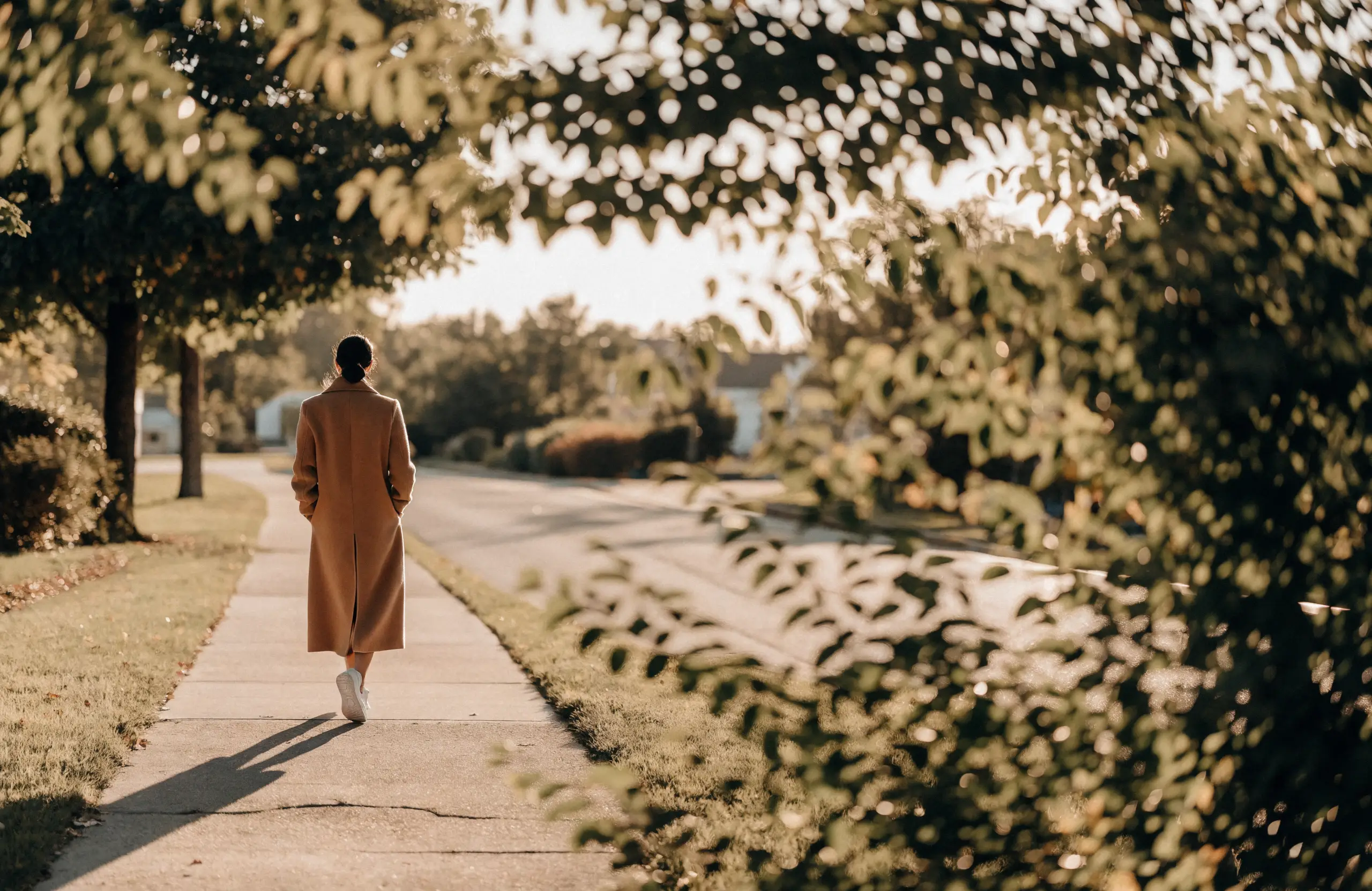 A woman walking a quiet tree-lined sidewalk at golden hour