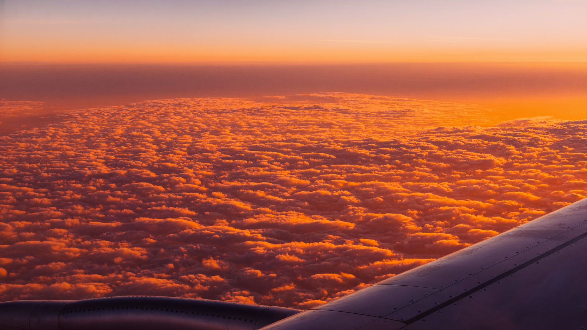 Plane wing above clouds at sunset, aerial view from a window seat
