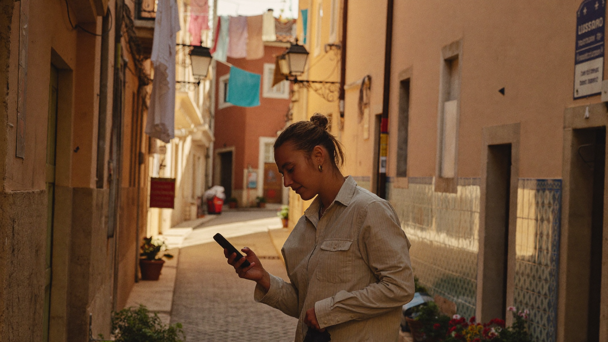 Narrow cobblestone alley in Lisbon, Portugal, warm evening light, a traveller walking and looking at their phone