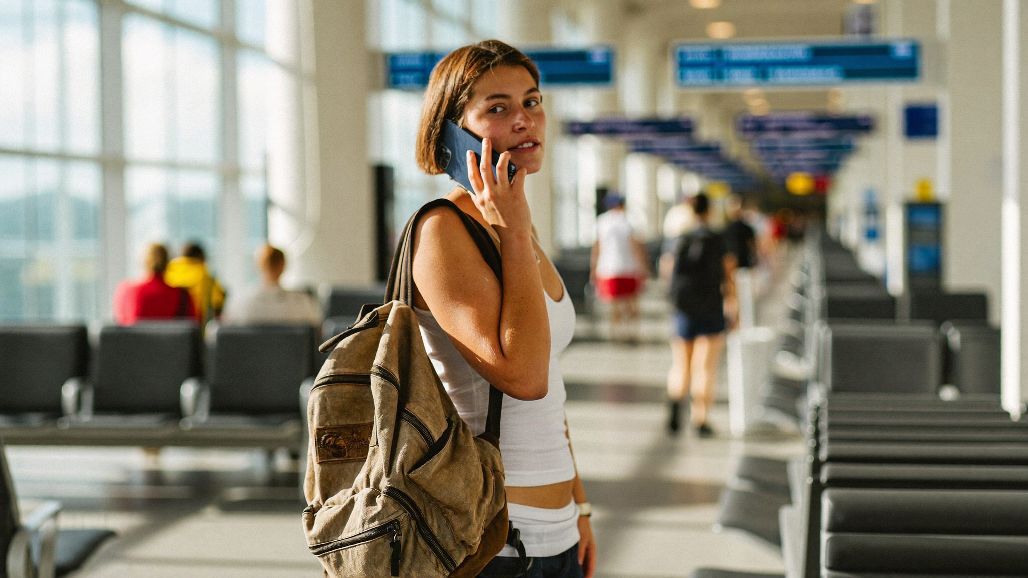 Backpacker speaking on a phone call in an airport departure hall, looking calm and reassured