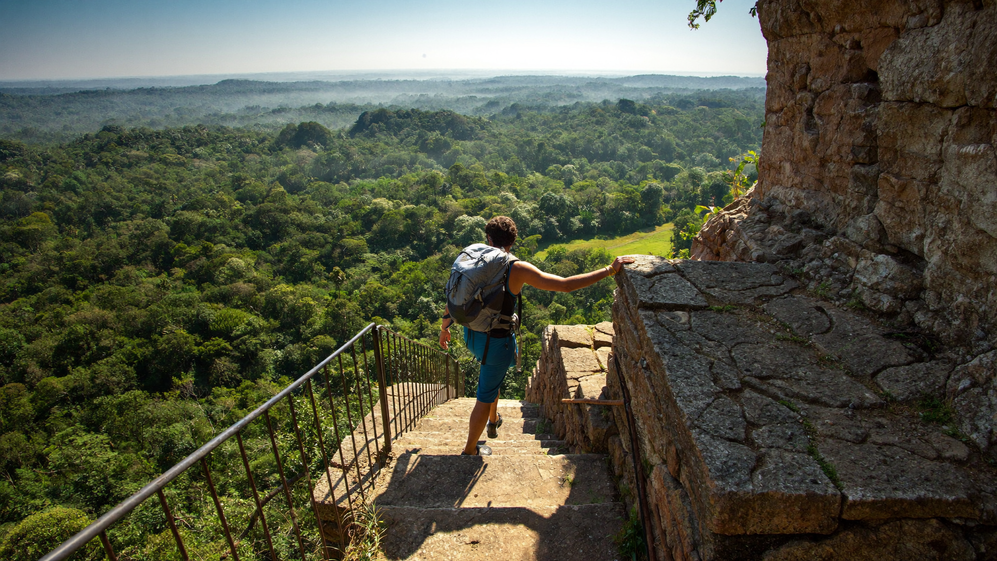 Solo traveller climbing the ancient staircase of Sigiriya Rock Fortress, jungle spread below, no visible device screens