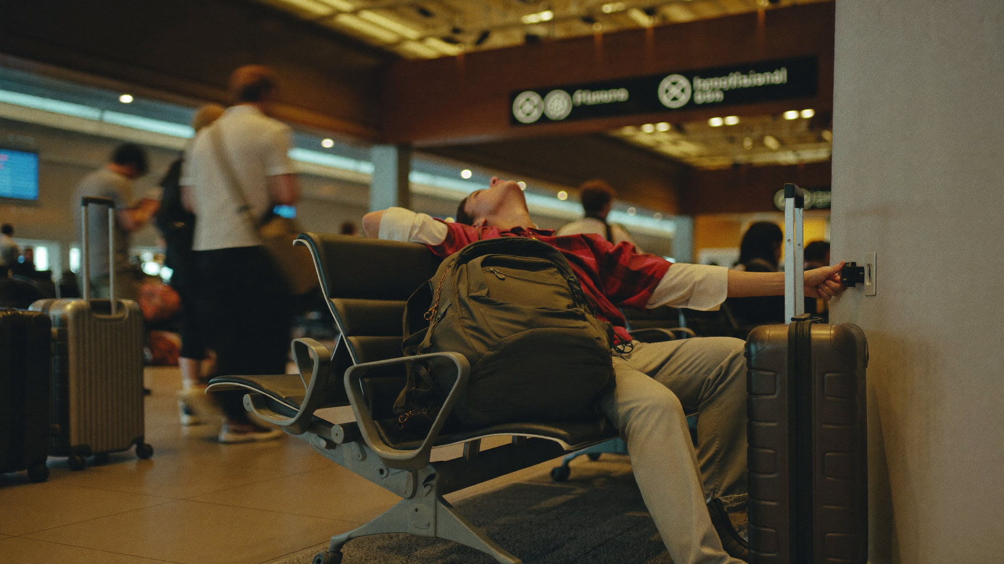 Tired traveller searching for a power outlet at a busy airport terminal, bags at their feet