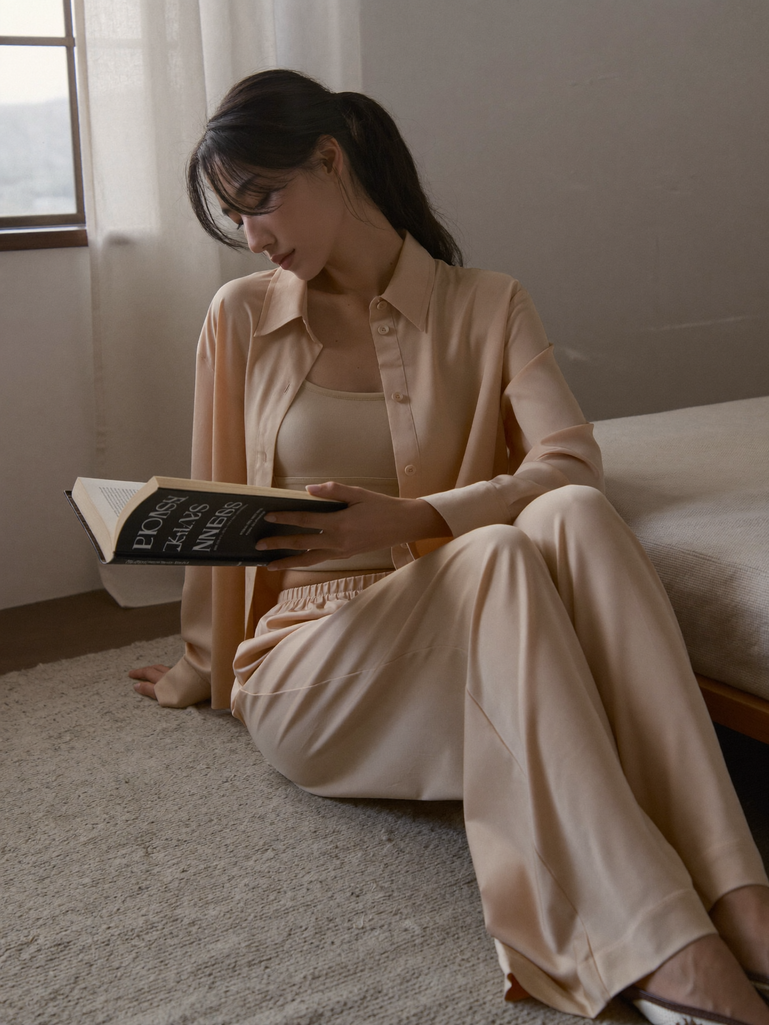 Femme lisant dans son ensemble loungewear sable près d'une fenêtre