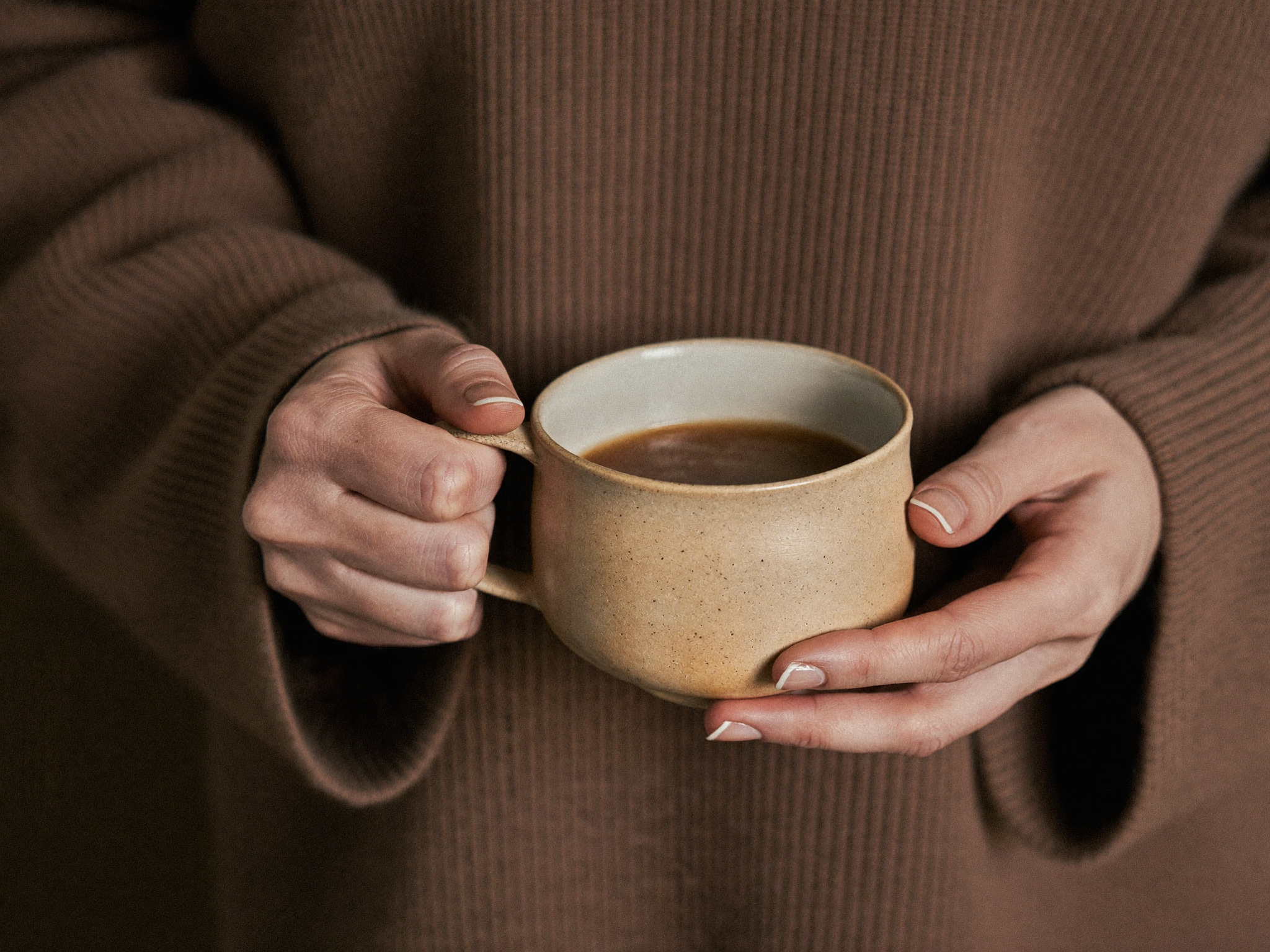 Mains tenant une tasse chaude avec une manche en tricot côtelé cacao