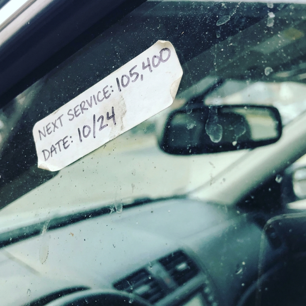 A sun-faded oil change reminder sticker in the corner of a windshield, months past due