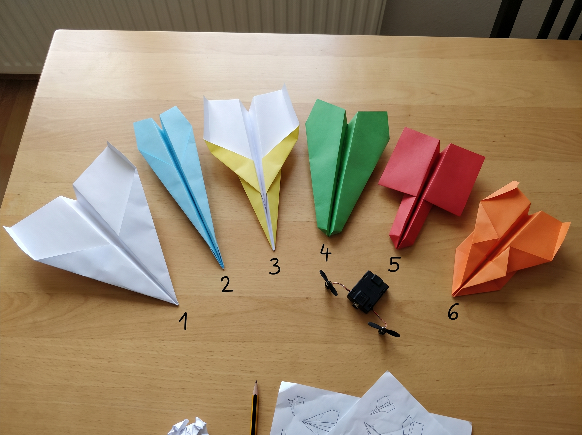 Six different paper plane designs with numbers written on the wings, ready to test