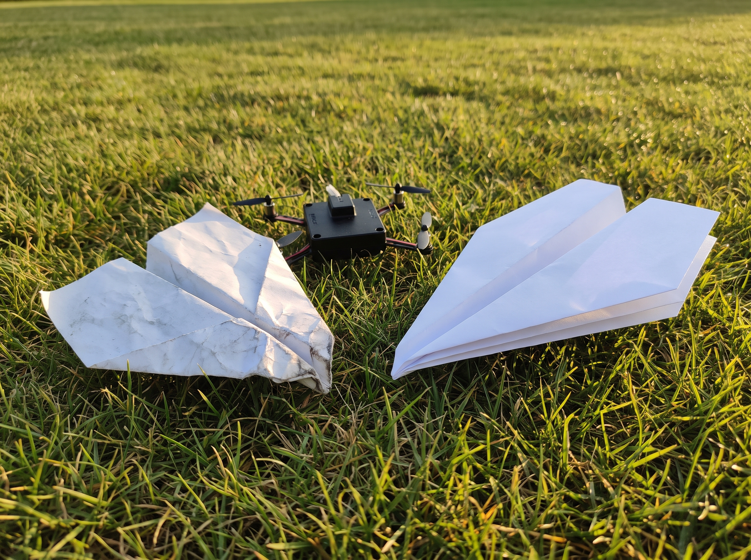 The paper crumples, the motor doesn't — a wrecked plane beside the undamaged module and a stack of fresh planes