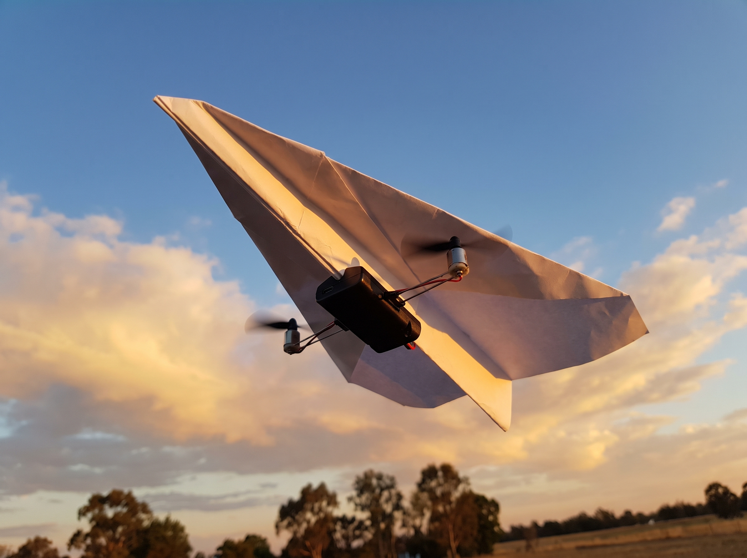 The folded paper plane climbing and banking under power, propellers spinning