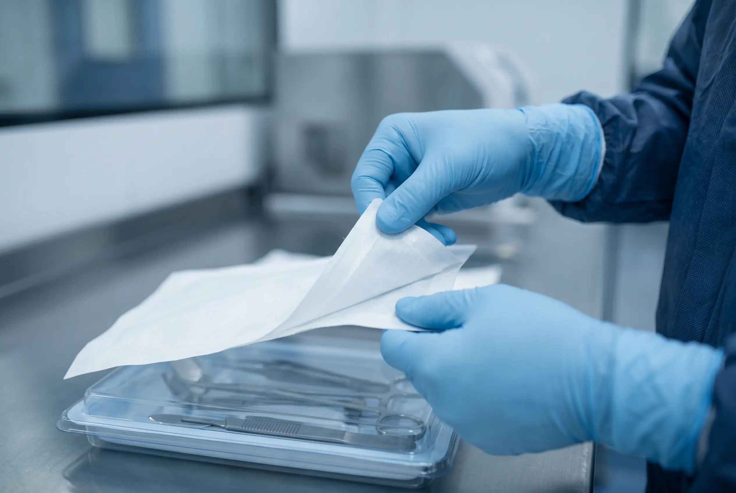 Gloved hands peeling a sterile lid from an instrument tray