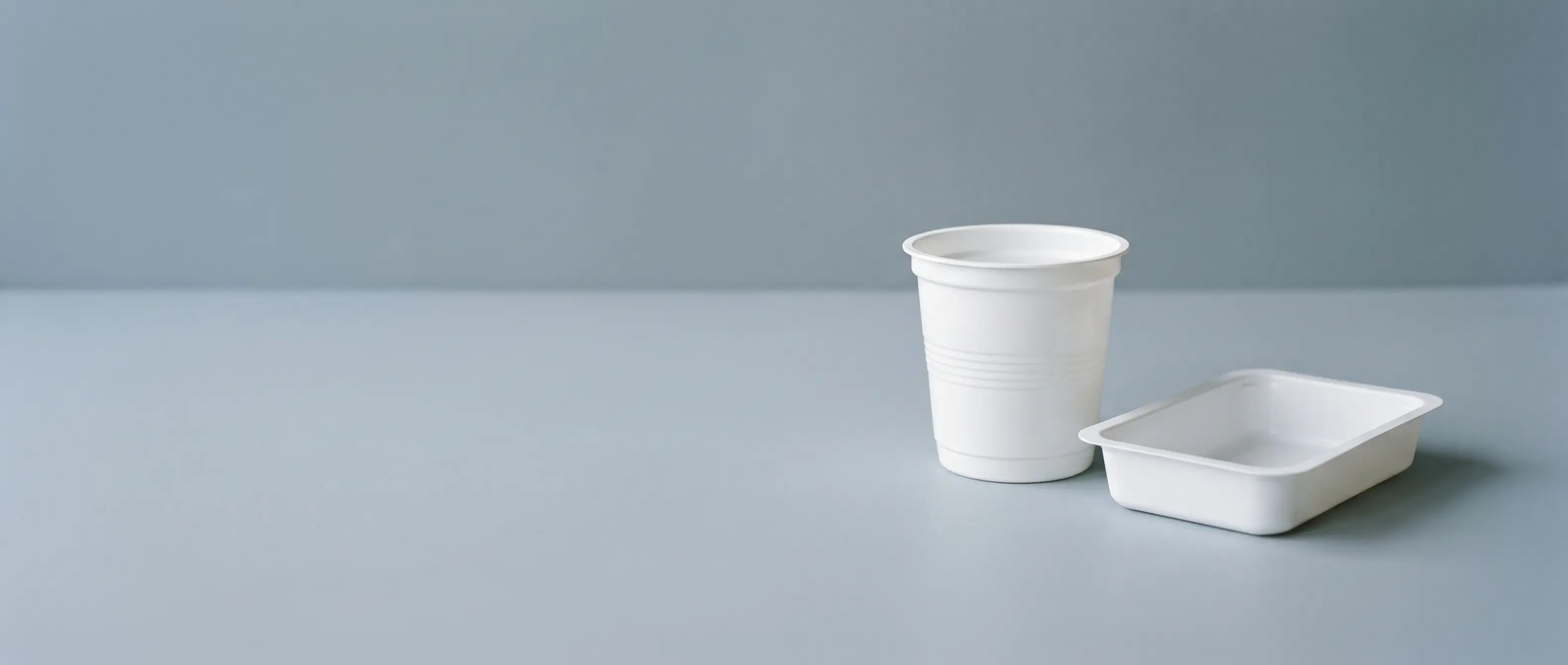 Thermoformed polystyrene packaging — a clear GPPS retail blister beside tough opaque HIPS trays and cups