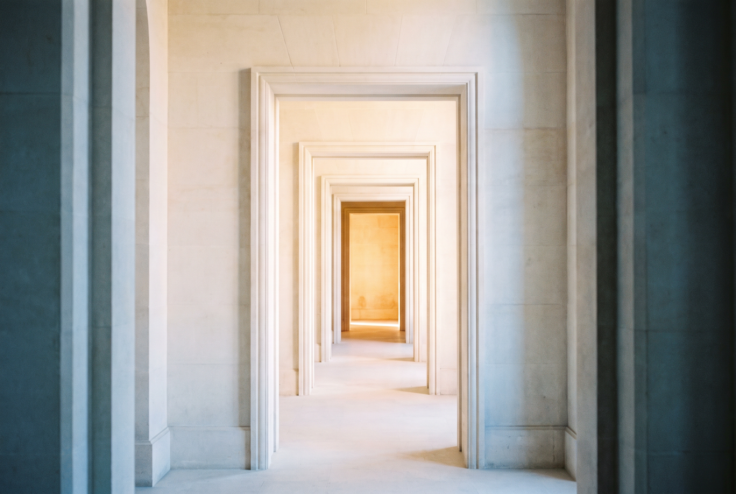A long enfilade of pale limestone doorways receding toward one filled with warm daylight