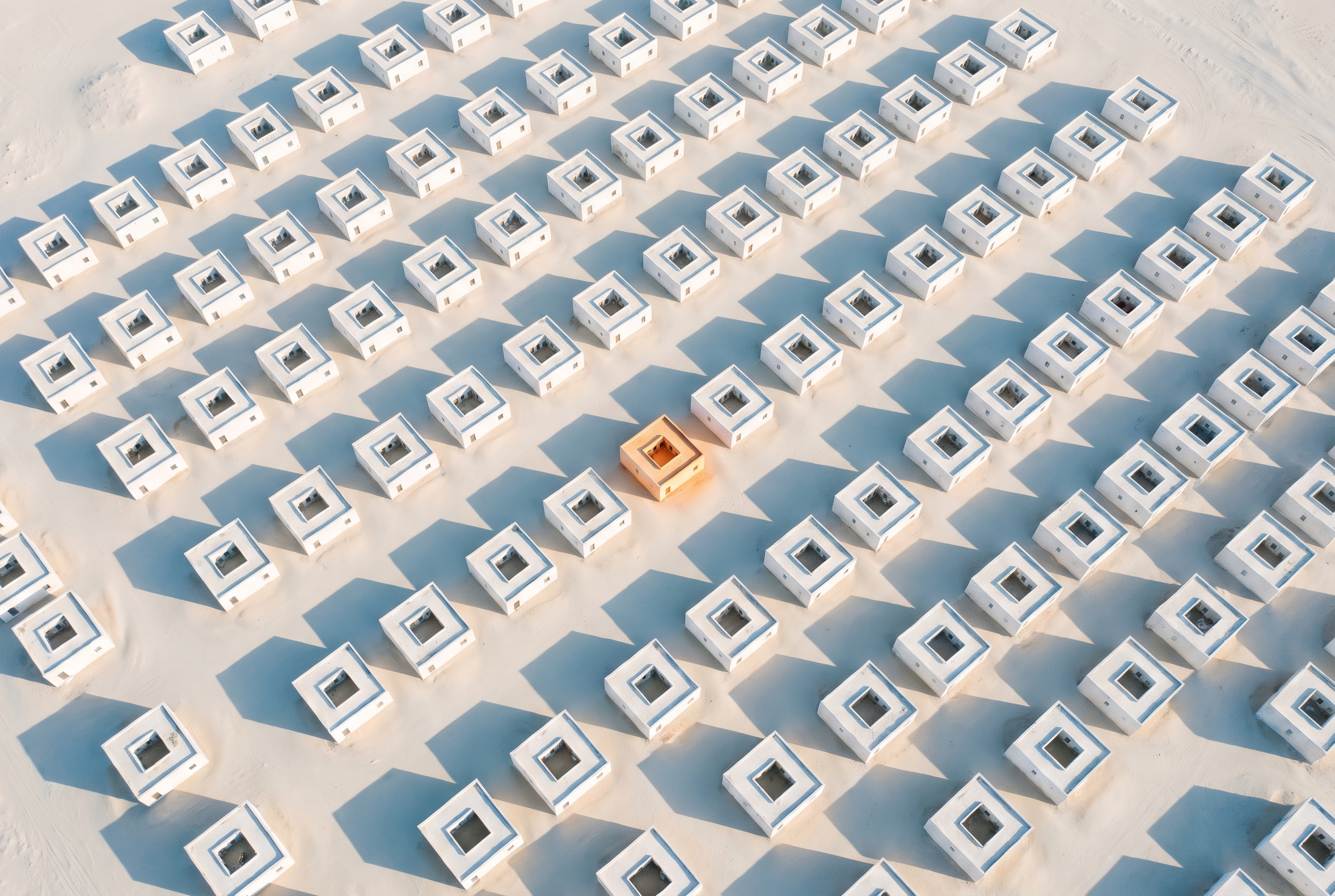Aerial view of a grid of small white courtyard buildings with one courtyard glowing warm