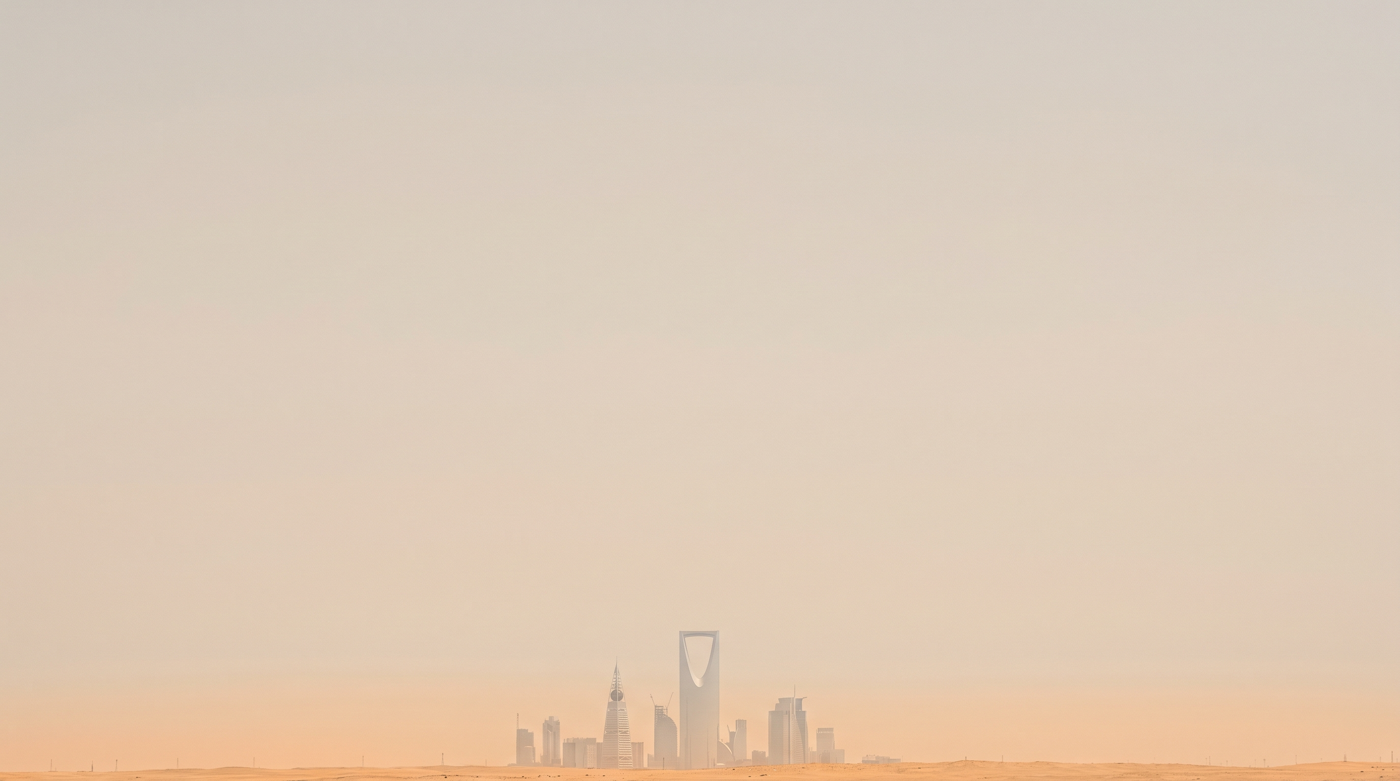 Riyadh towers at midday seen through fine desert haze under a vast pale sky