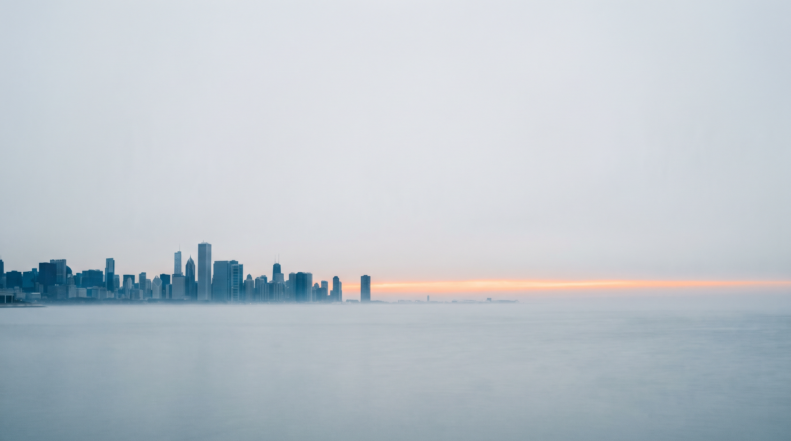 An American skyline at dawn across open water with a warm sliver of sunrise