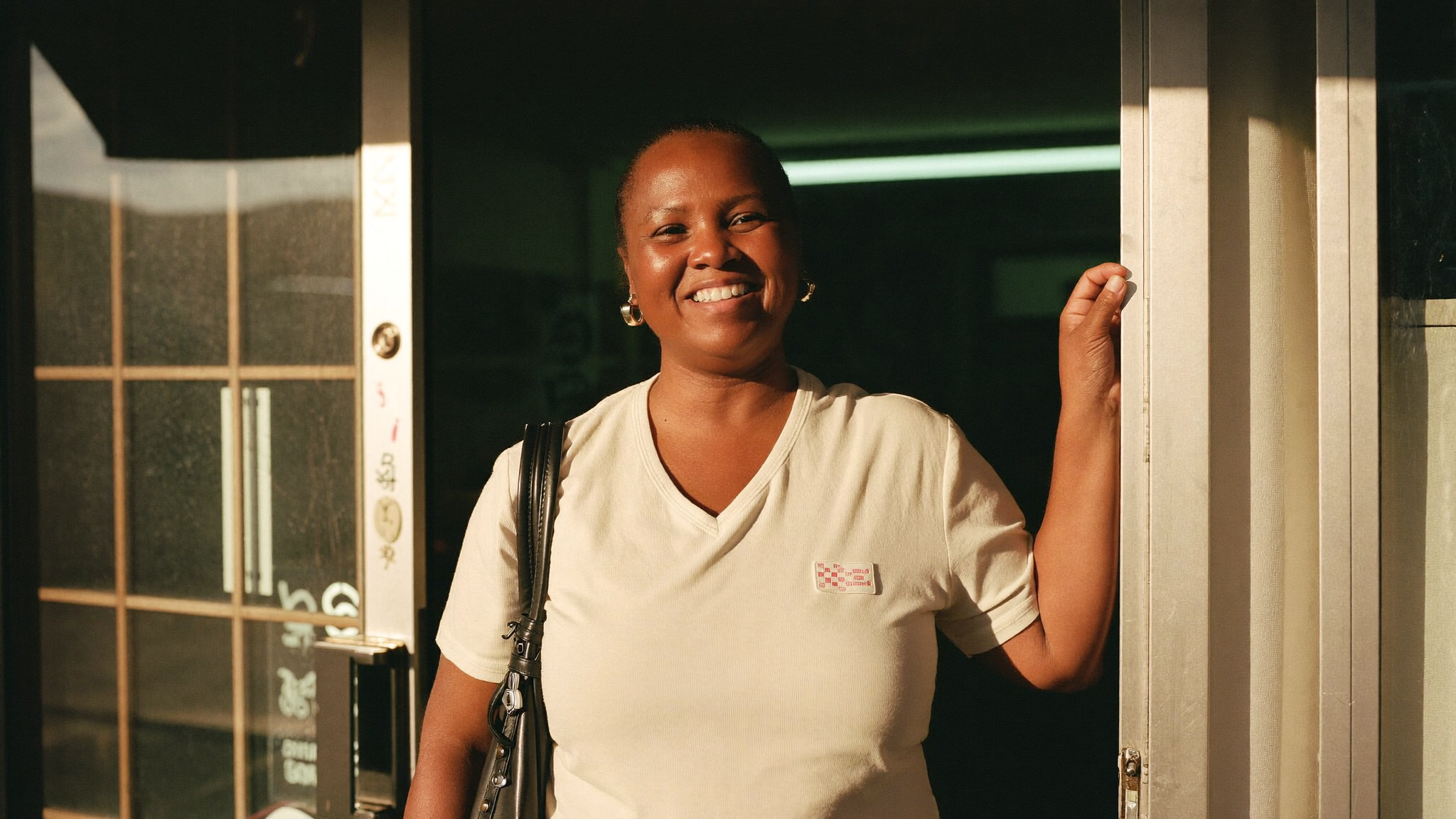 A small business owner standing in the doorway of her shop at golden hour