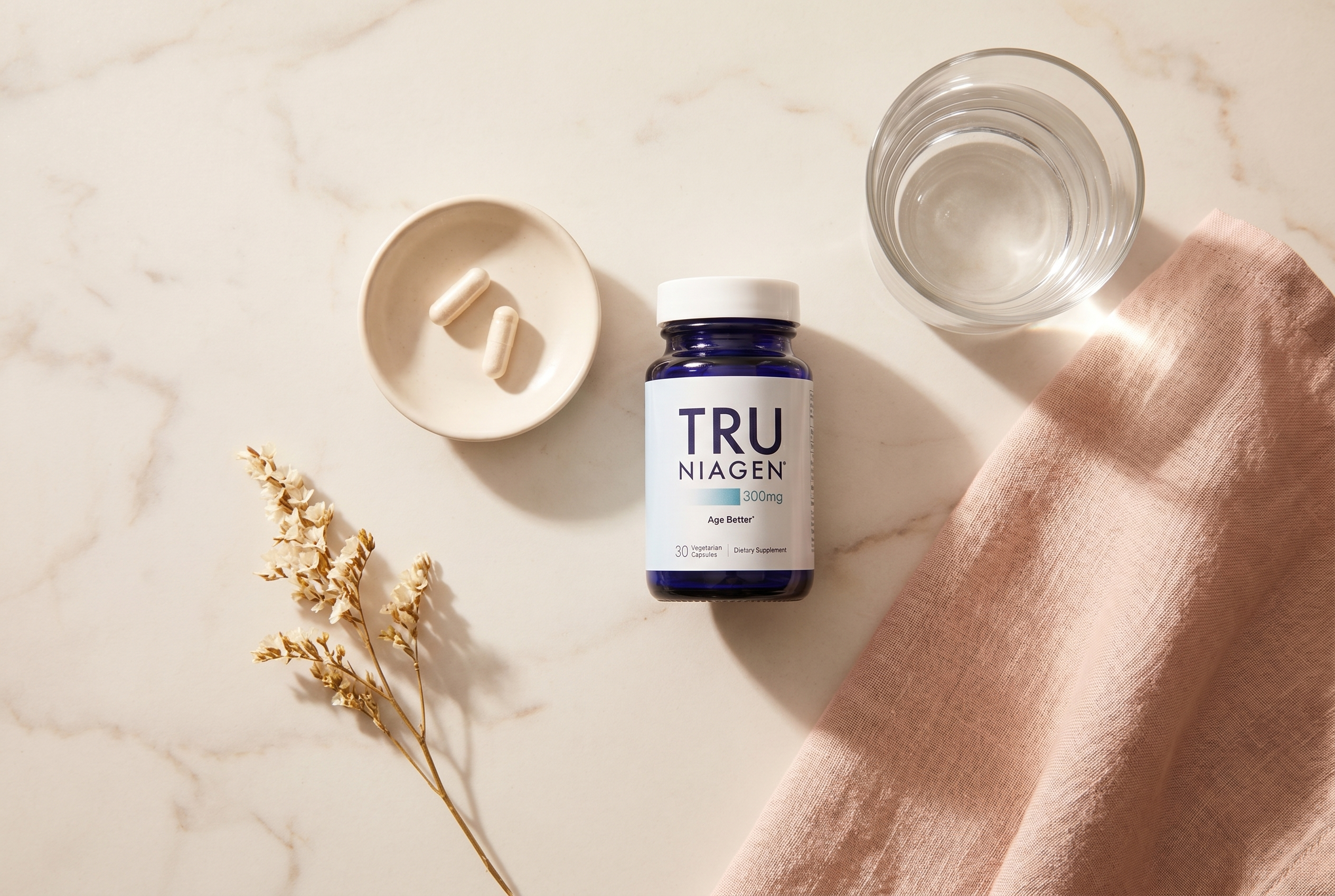 Tru Niagen 300mg bottle with cream capsules in a warm editorial flat-lay on a sunlit marble counter