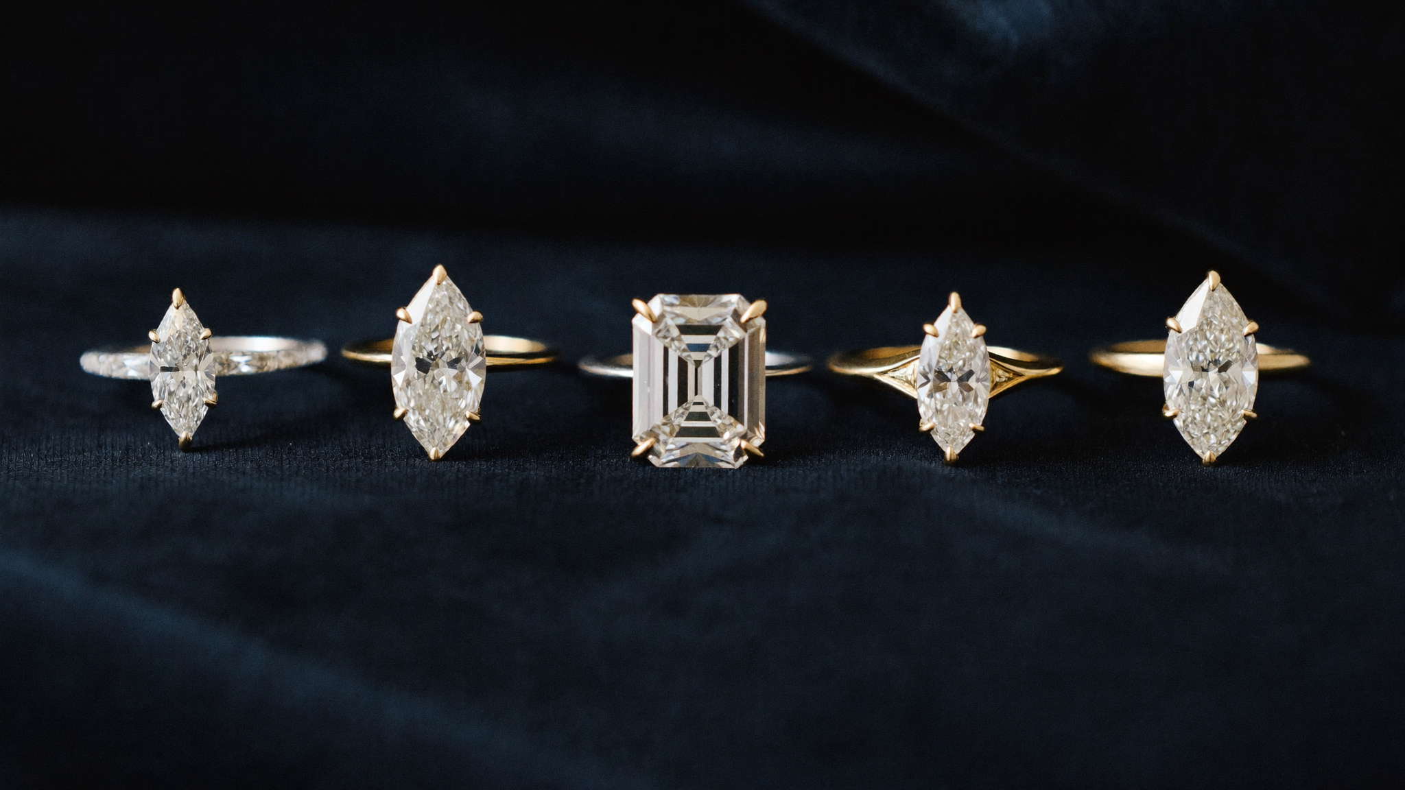 Five diamond cuts round, oval, emerald, pear, and marquise arranged on dark velvet under soft directional light