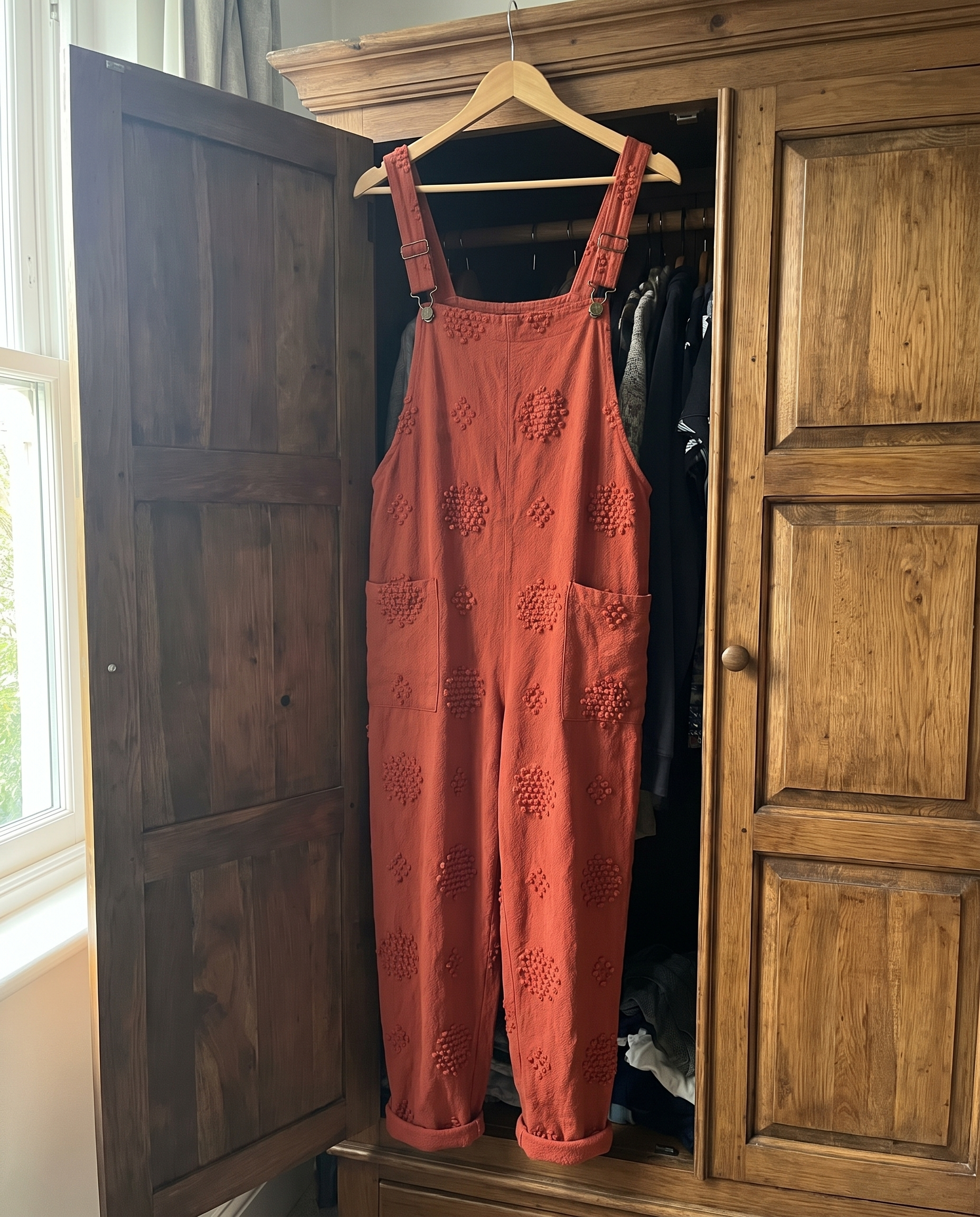 Flora Brick Red Jumpsuit hanging on a wooden hanger