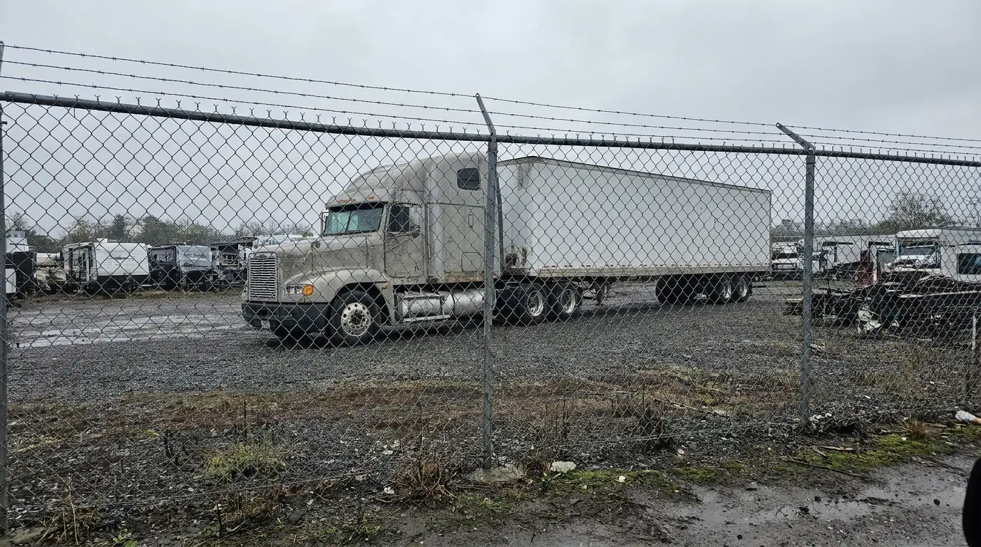 A tractor and dry van trailer parked behind a chain link fence inside an impound yard, the situation no truck insurance policy pays a driver to sit through.