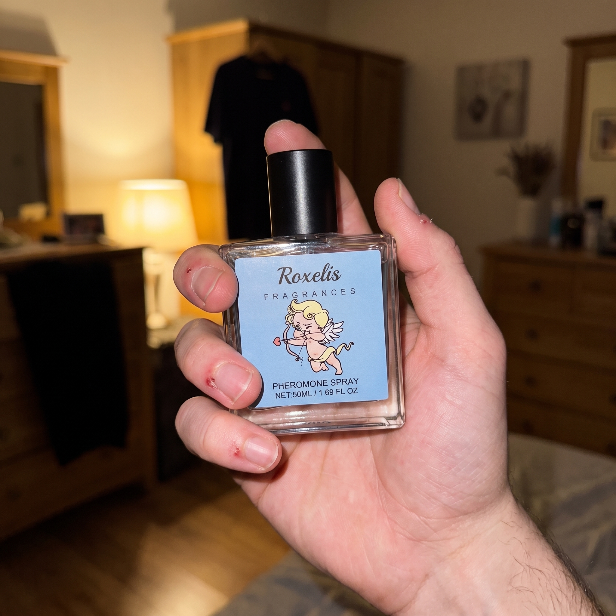 A close-up of a hand holding the Roxelis pheromone cologne bottle in warm ambient light.