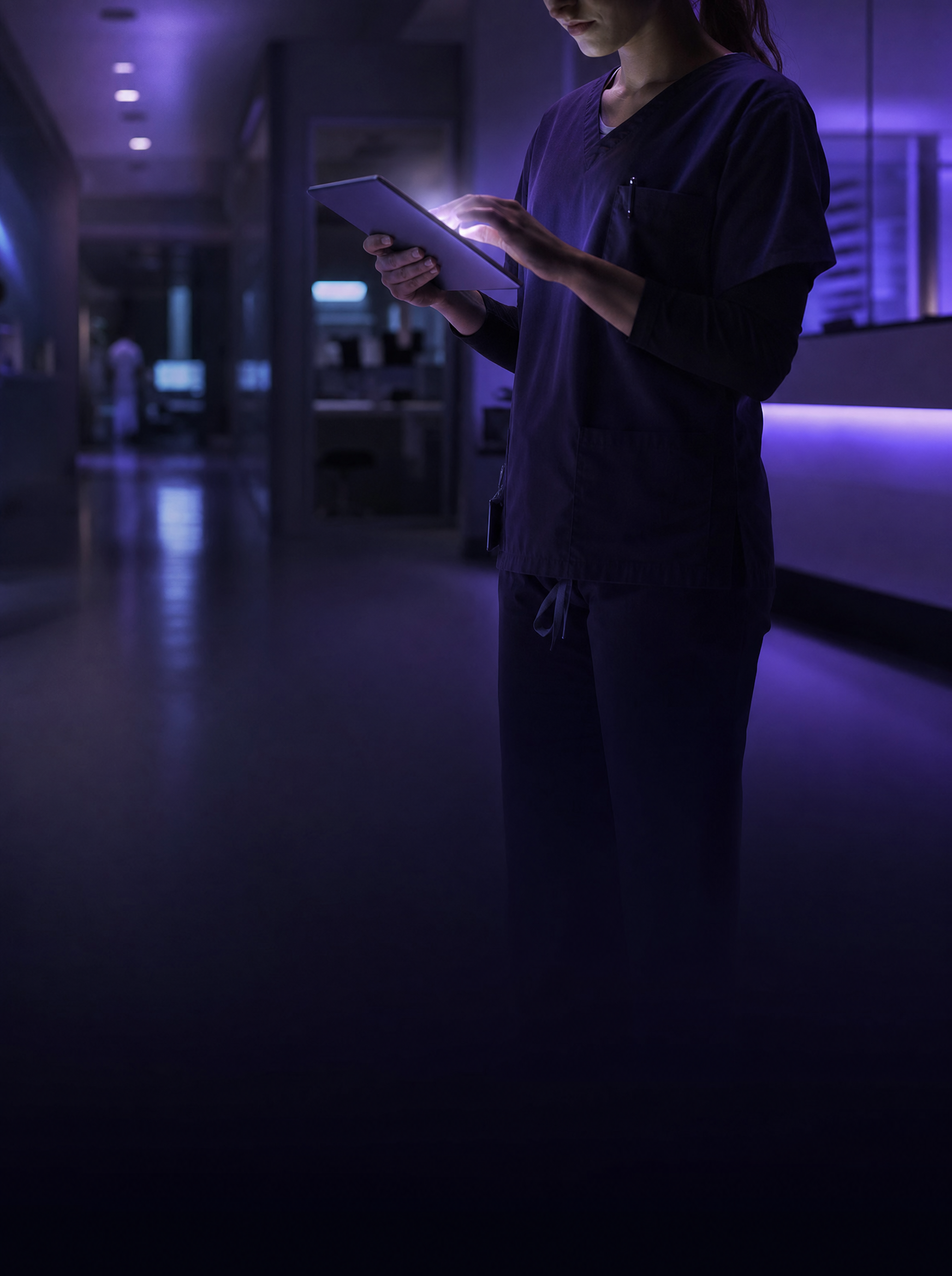 Clinician using a tablet in a dark clinical corridor
