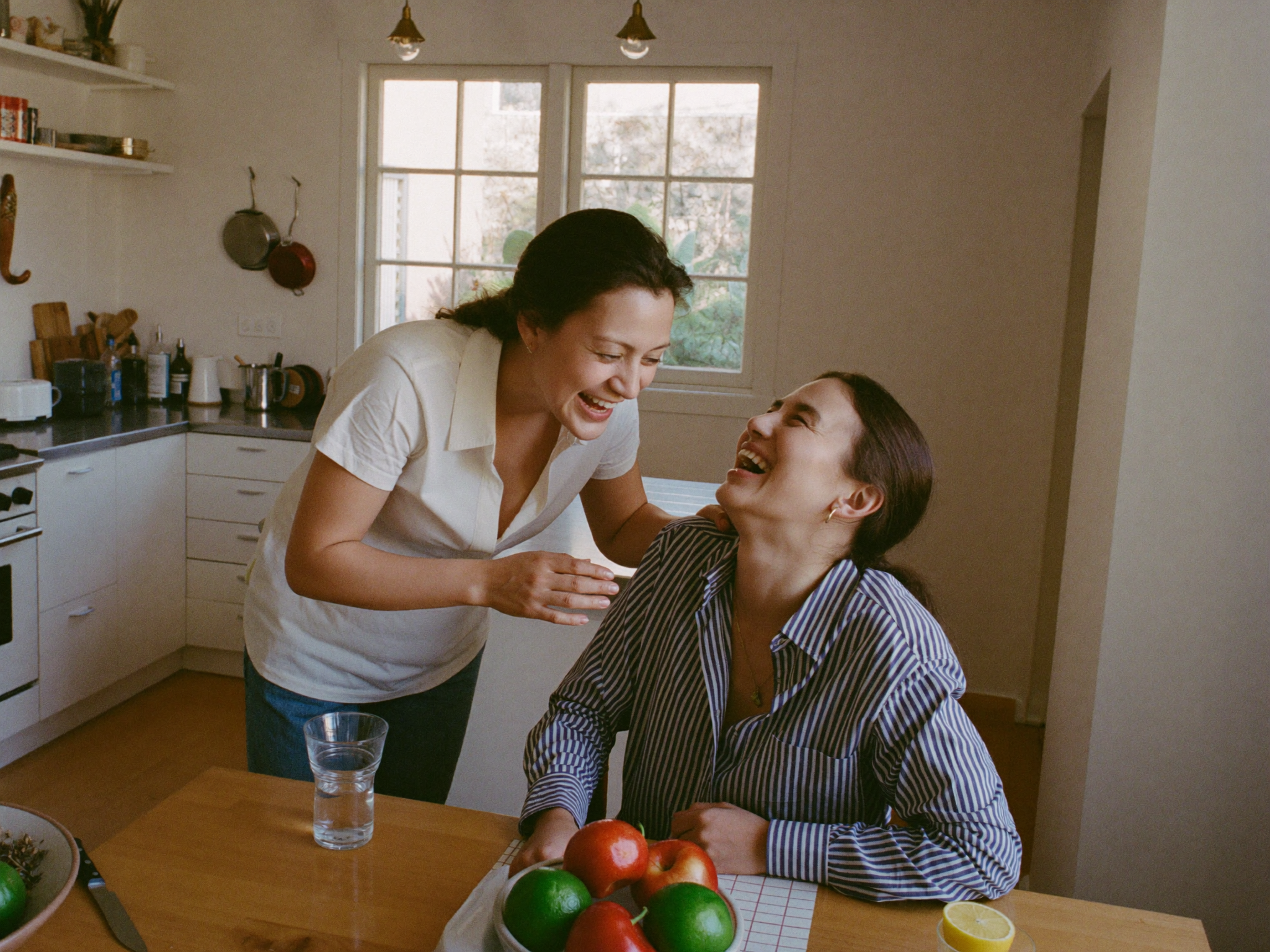 A mother and her teenage daughter laughing together in the kitchen in the morning